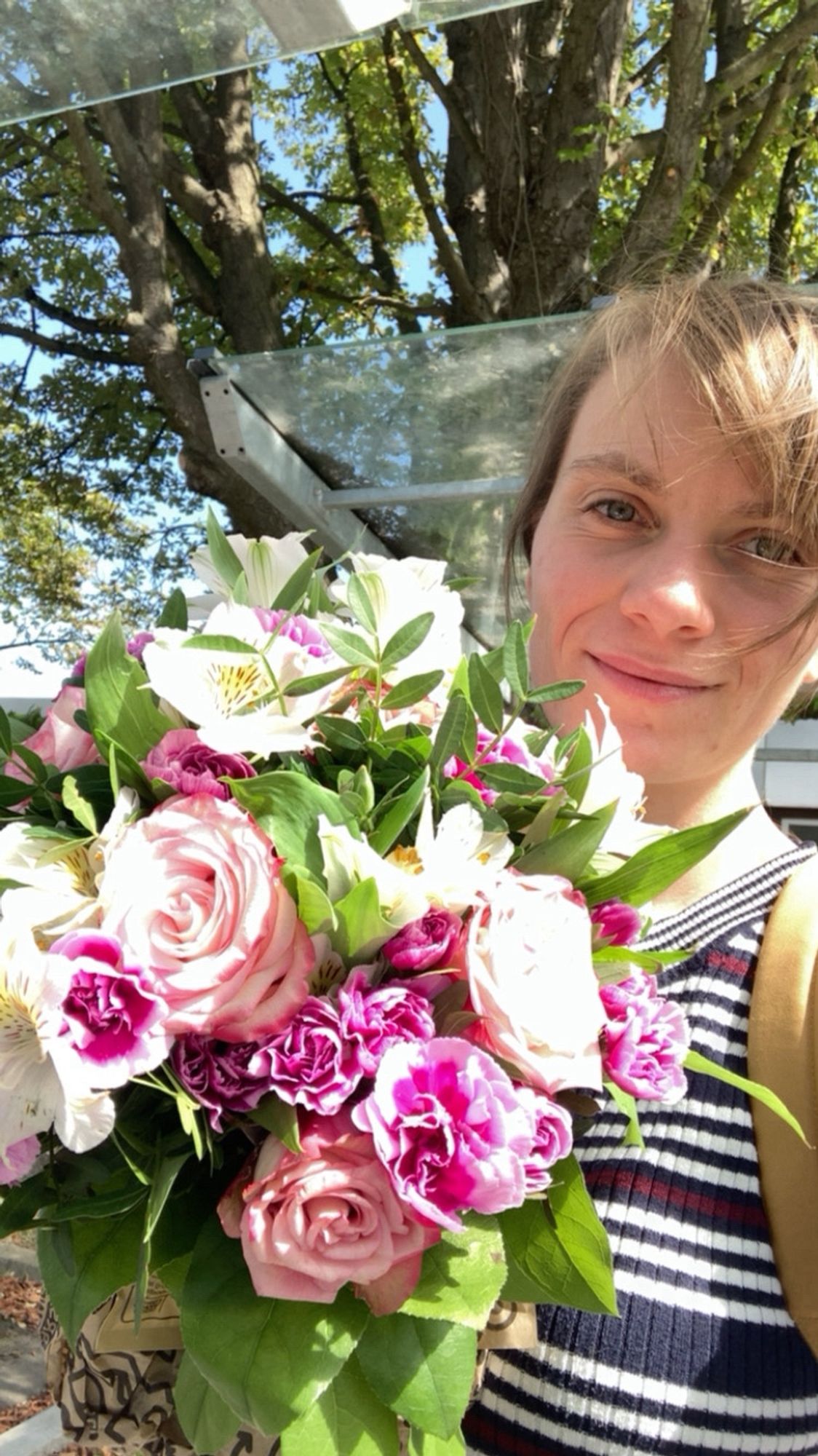 Ich (Frau Anfang 30, dunkelblonde Haare, dunkelblaues T-Shirt mit weißen Streifen) halte draußen bei Sonnenschein einen großen Blumenstrauß mit weißen, rosa und pinken Blumen in die Kamera