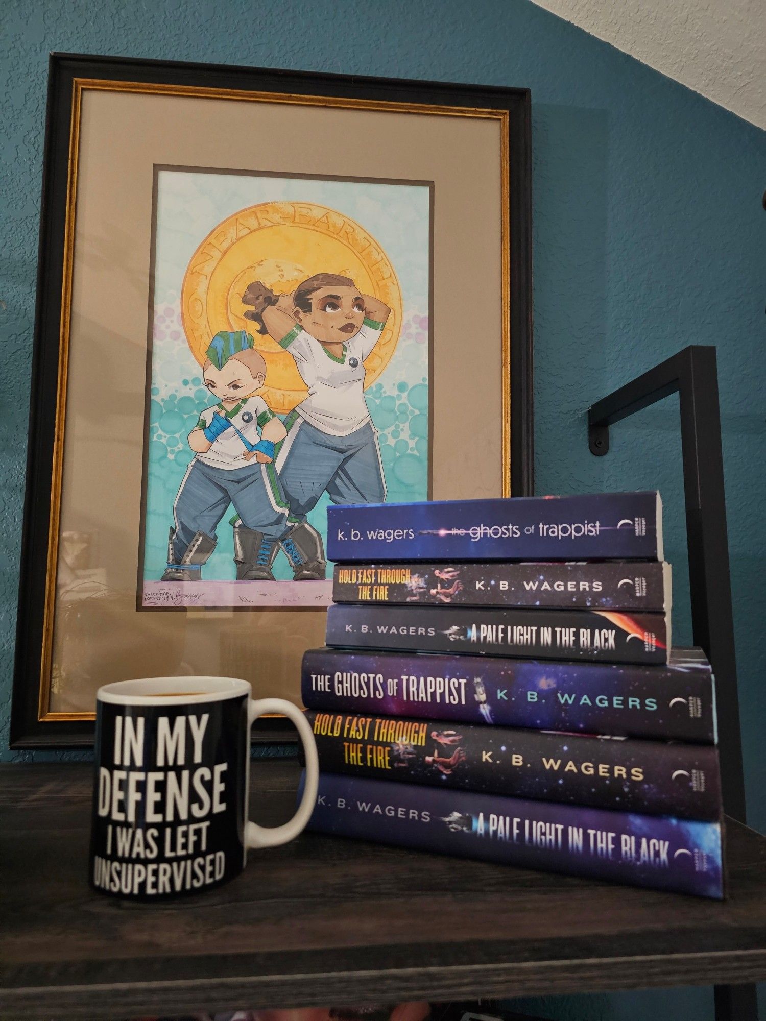 Photograph of a black and white mug on a shelf next to a stack of NeoG books in both paperback and hardcover. They are space opera with blue, black, purple colors.

Mug text: In my defense I was left unsupervised 
Book texts: A Pale light in the Black
Hold Fast Through the Fire
The Ghosts of Trappist 
All by K.B. Wagers

A drawing in the background of two women in matching blue tack pants and white shirts are getting ready for a fight. The taller is tying her hair back and the shorter is wrapping her fists in boxing wraps.