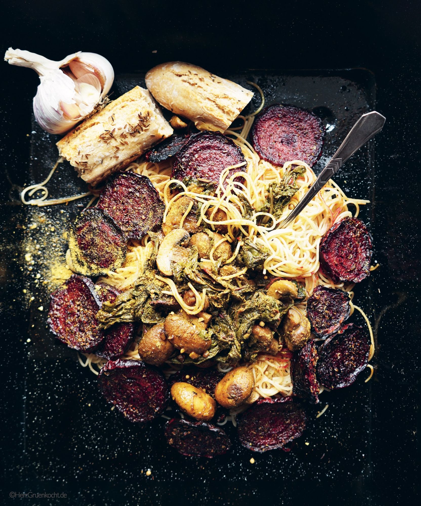 Schwarzer Untergrund. Darauf: Spaghettini mit geschmorter Roter Bete, Mangold und Pilzen.