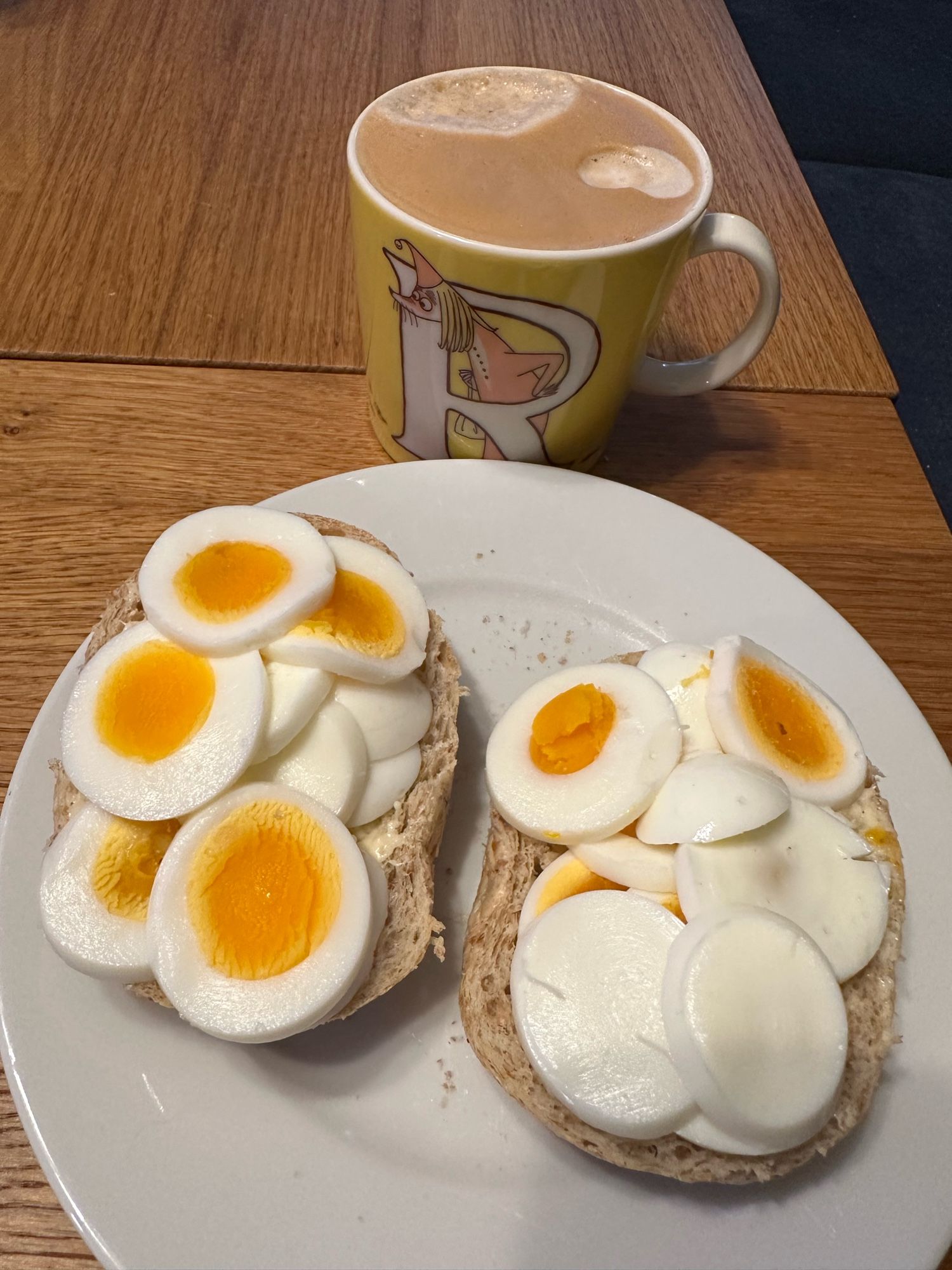 To halve rundstykker med kokt egg og en kopp med kaffe med melk 