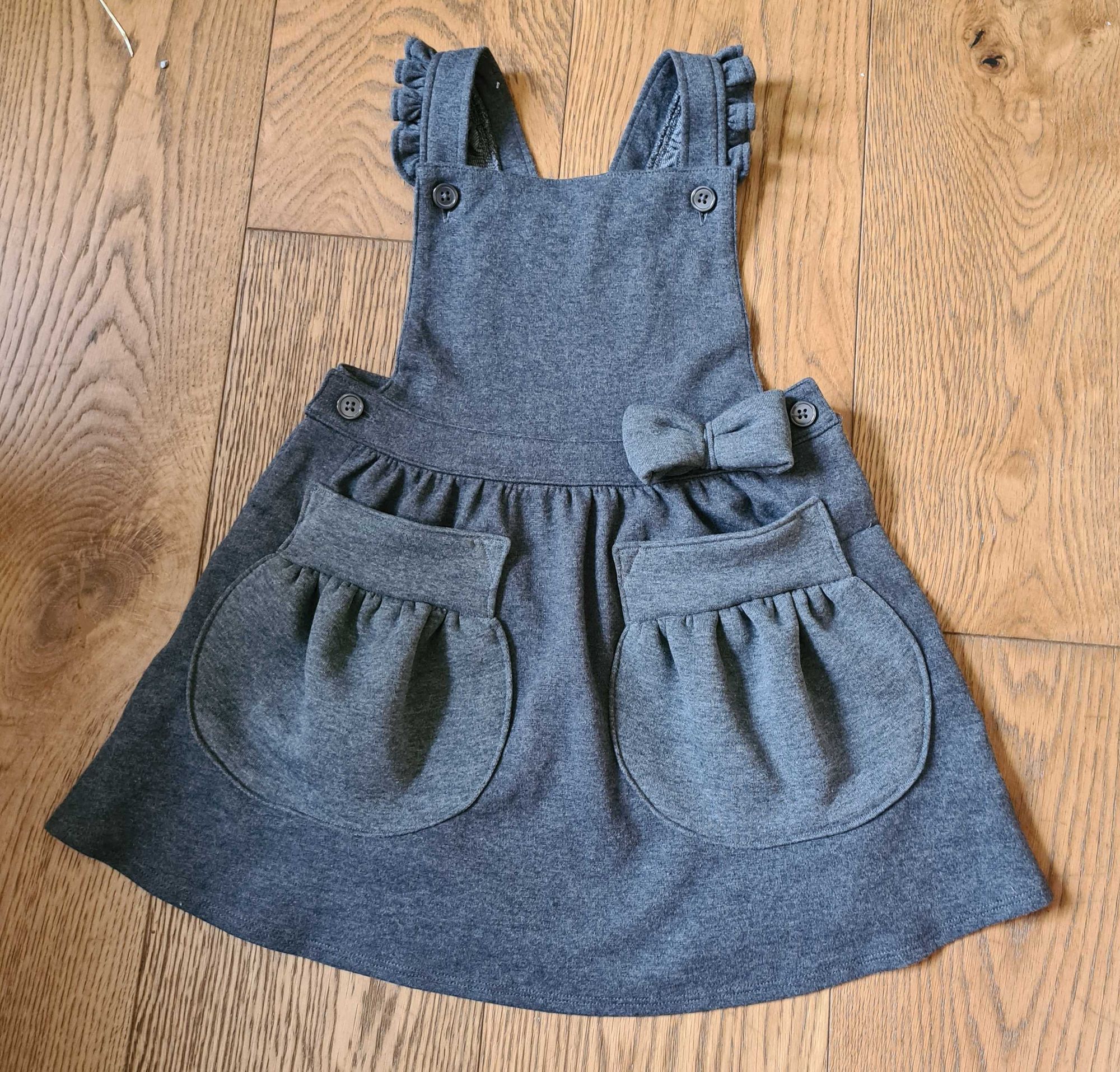 Grey pinafore school dress with big gathered patch pockets added to the skirt in a slightly different grey fabric