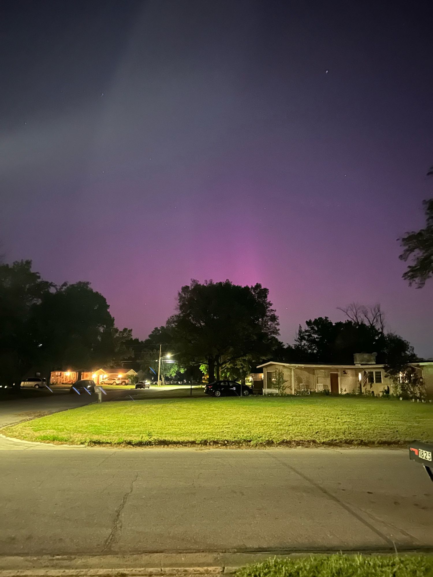 A house and yard and silhouette of trees against a pink/green gradient sky.