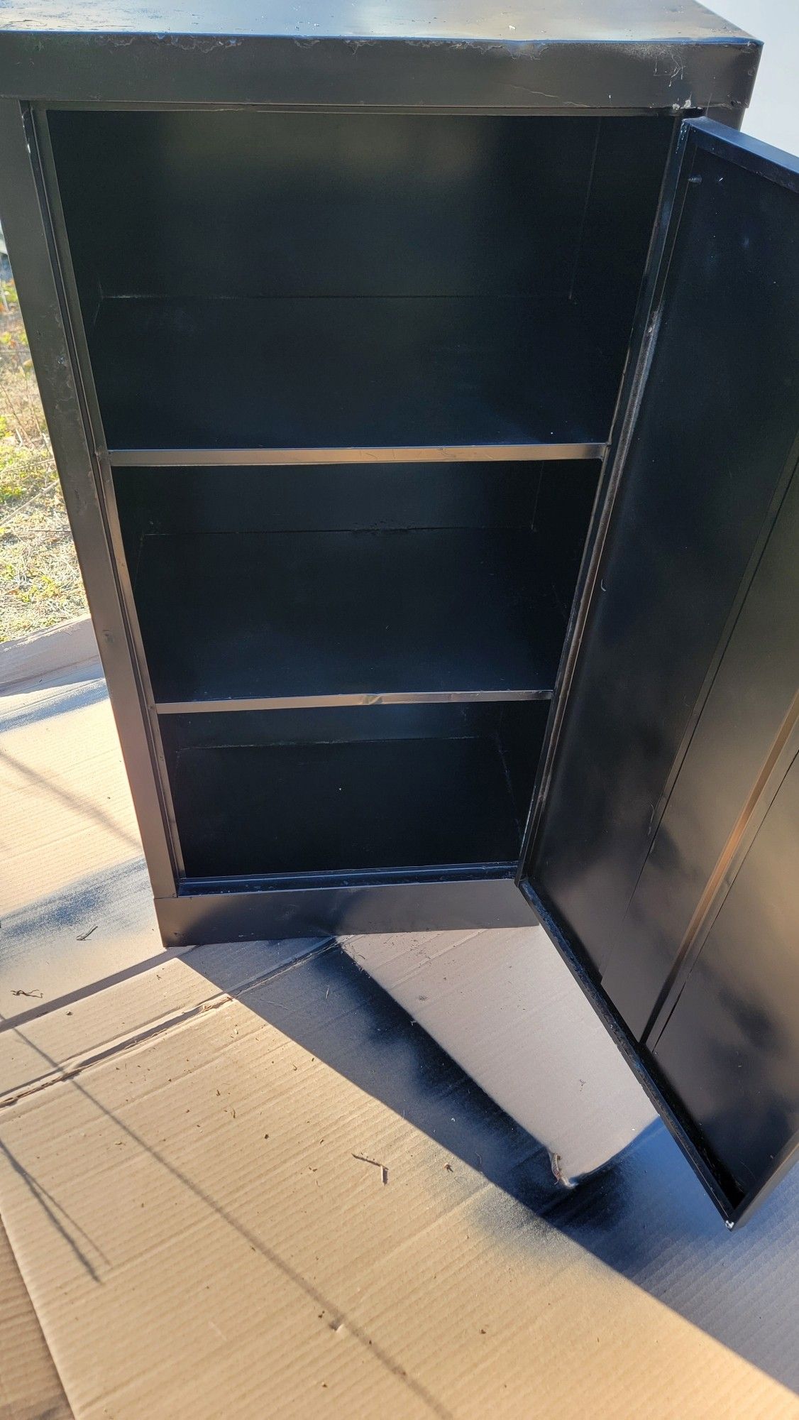 A metal cabinet painted black. There are 2 shelves on the inside. (3 storage spaces)