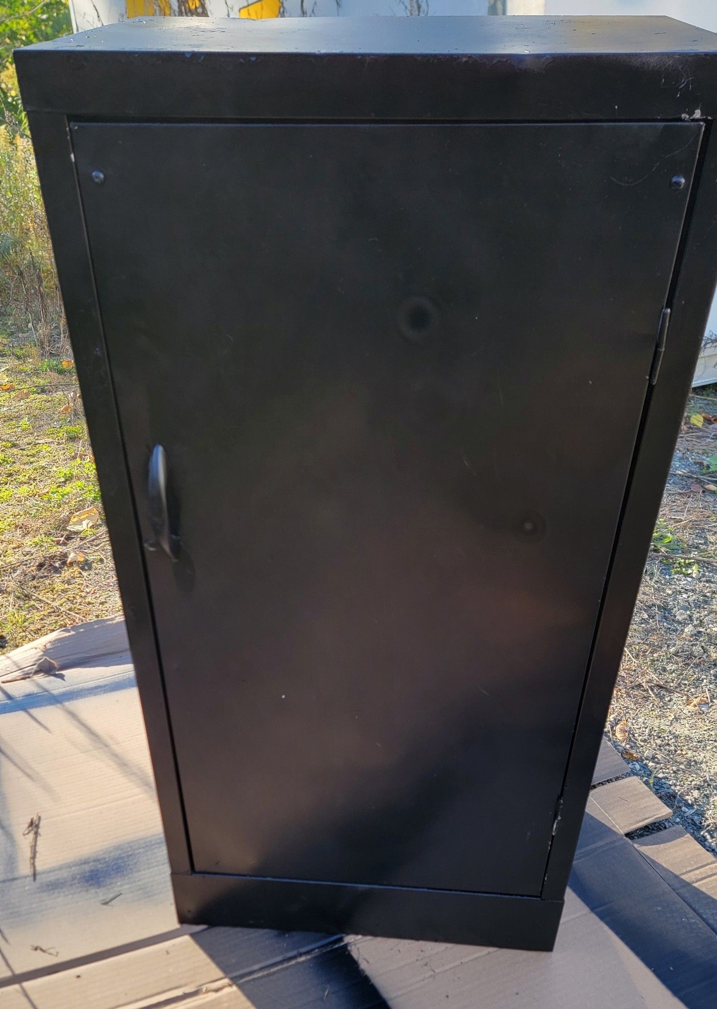 A metal cabinet painted black. There is a handle on the left-hand side.