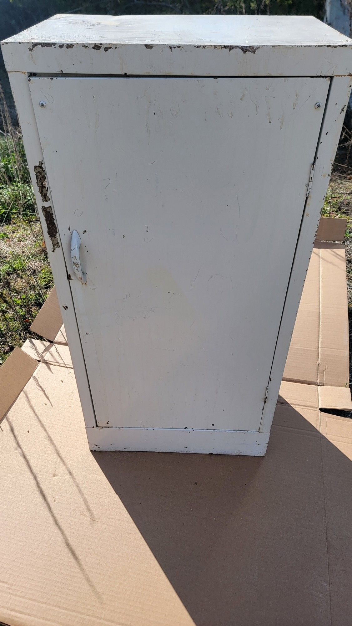 A metal cabinet painted white, looking a little worse for wear. There is a handle on the left-hand side.