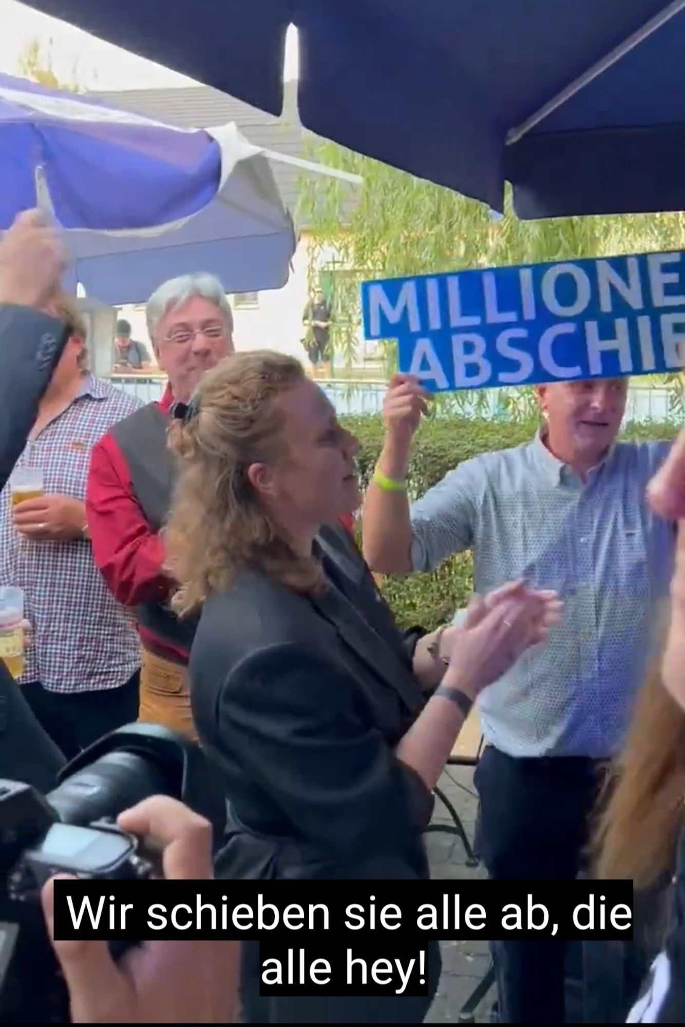 Bild aus den Video der AfD Wahlparty auf dem Wir schieben Sie alle an gesungen wird

Einer hält ein Schild hoch mit Millionenfach abschieben

Tassis steht fröhlich klatschend daneben und singt mit