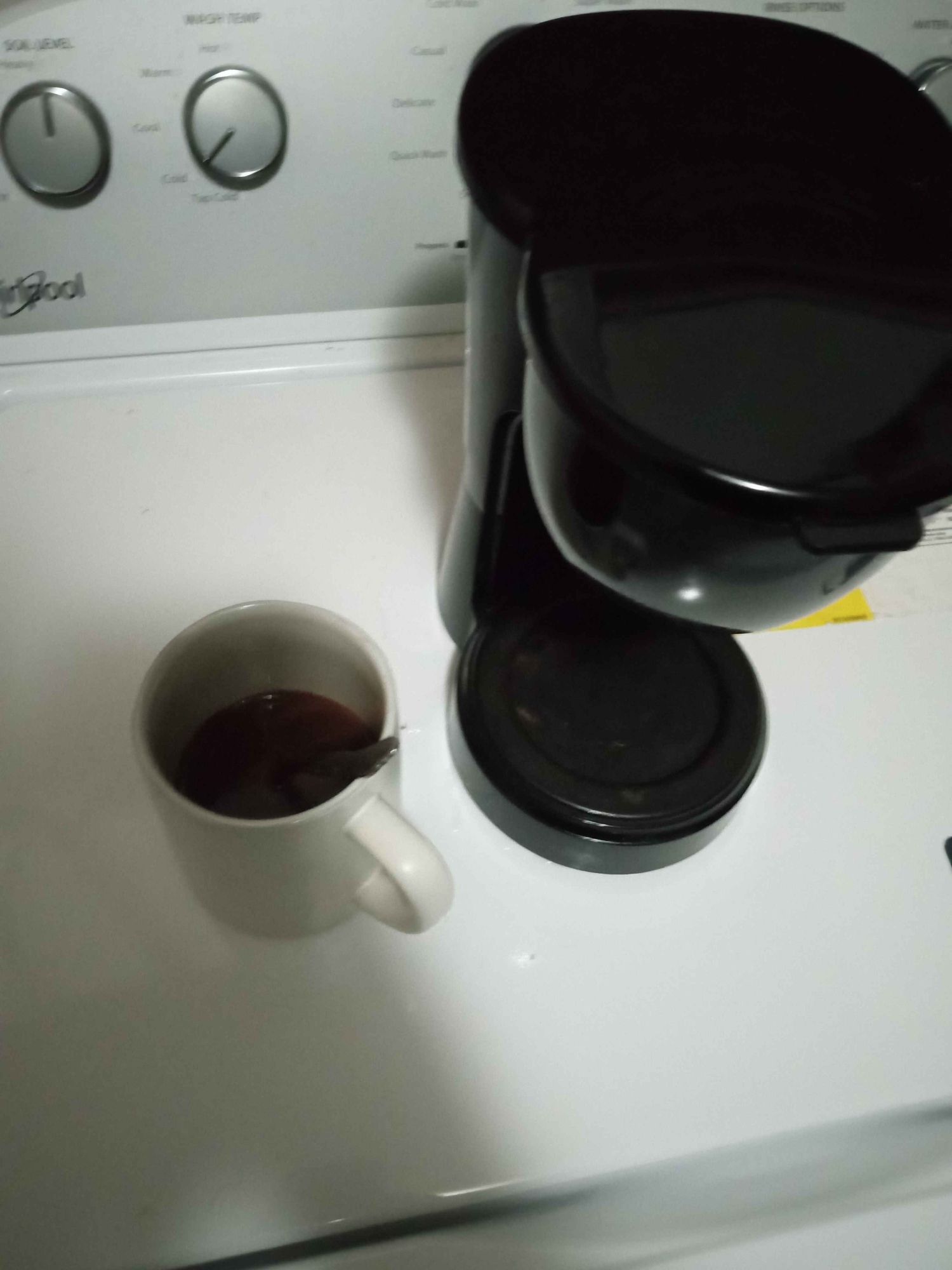 Great Value Brand Coffee Maker and coffee mug with spoon. 1/4 full coffee, on a washer.