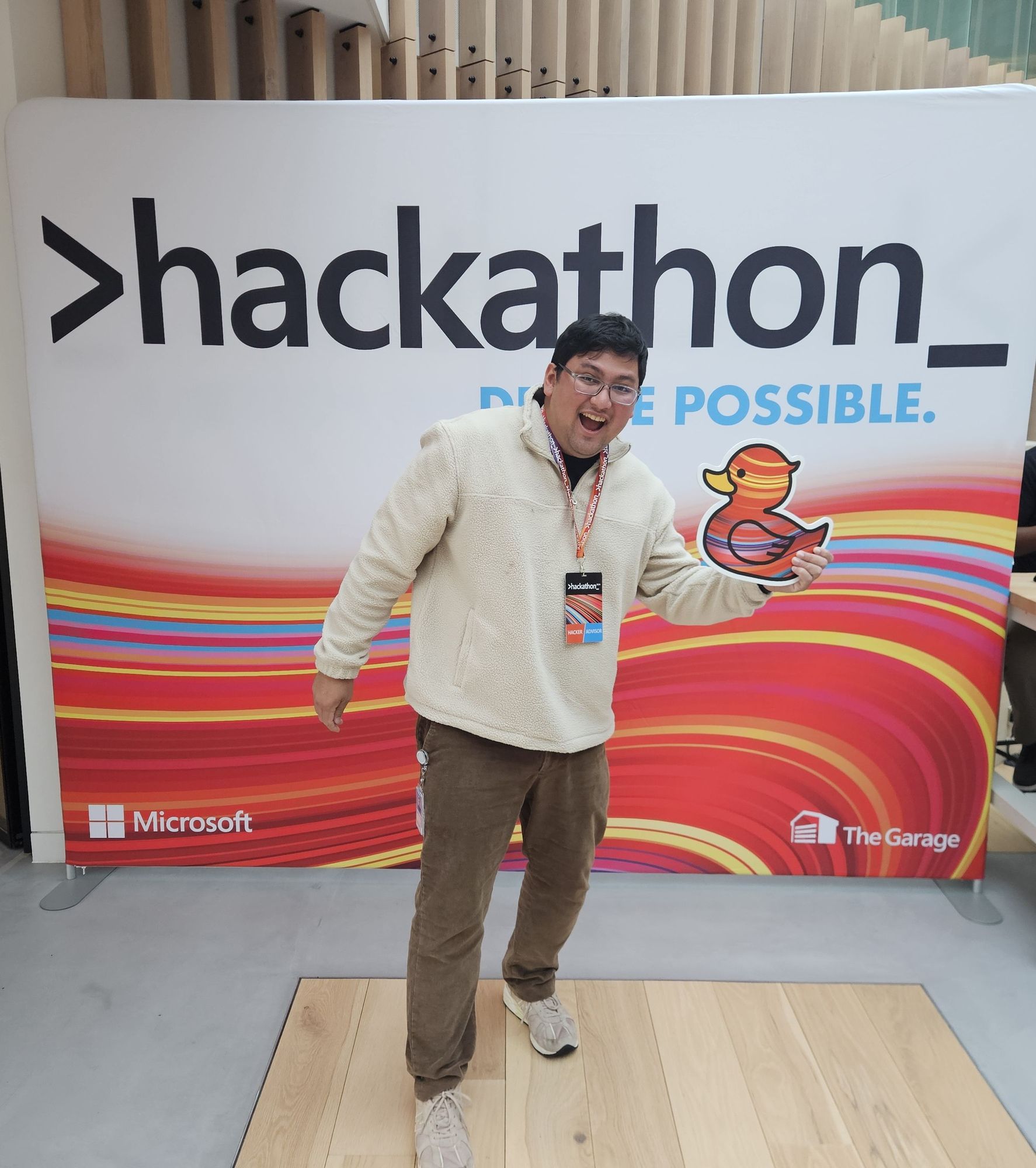 Men, black hair, medium height, in front of a panel with hackathon visual Identity on it and holding a plaque in format of a rub duck