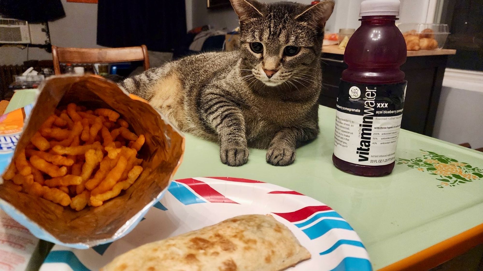 Cat on a kitchen table with a hot pocket, Cheetos and a vitamin water