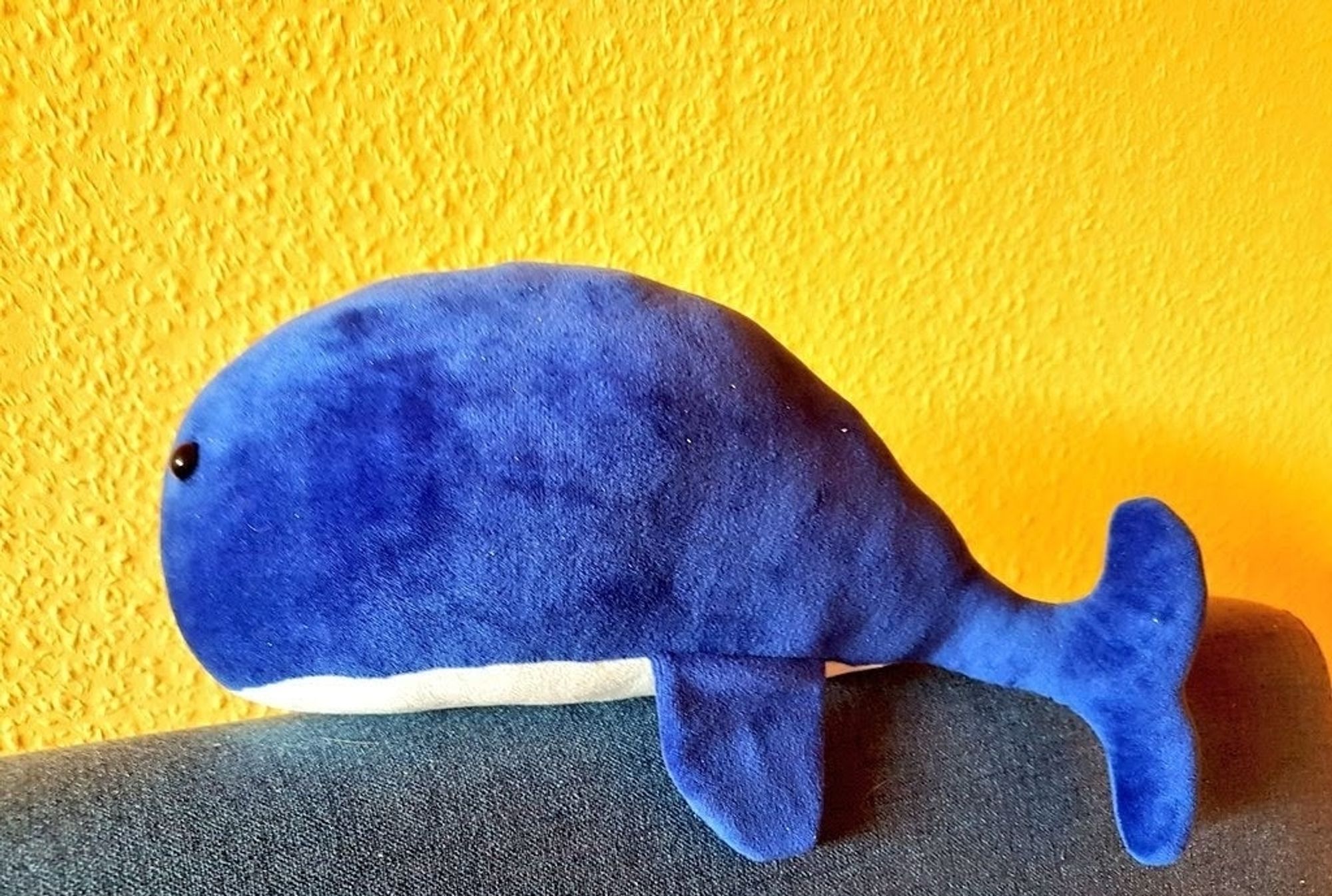 Blauer Plüschwalfisch des Sohnes einst auf dem Rand der Bettkopfstütze vor gelber Tapete.