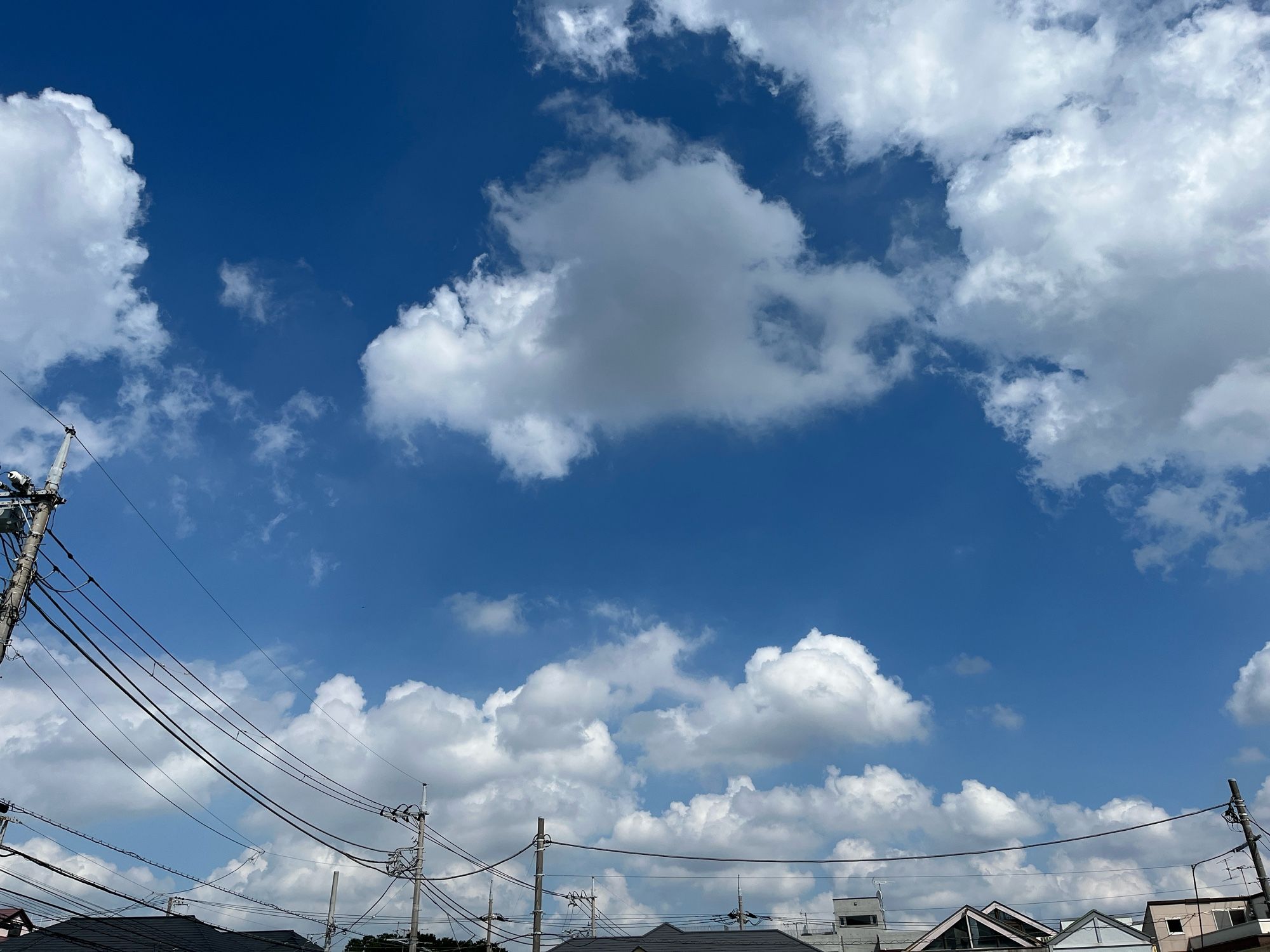 青い空に白い雲が浮かぶ様子。屋根や電信柱は太陽の光に照らされている。