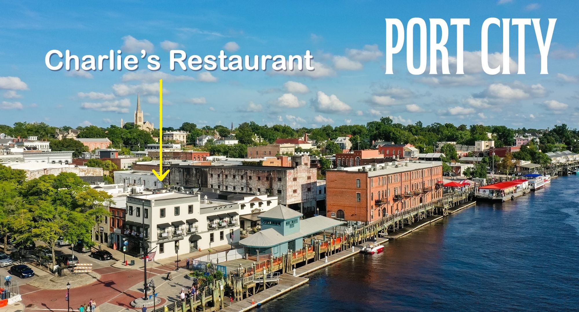 A picturesque riverside downtown area with old buildings, shops, restaurants on a main street, a river boardwalk, and the river.