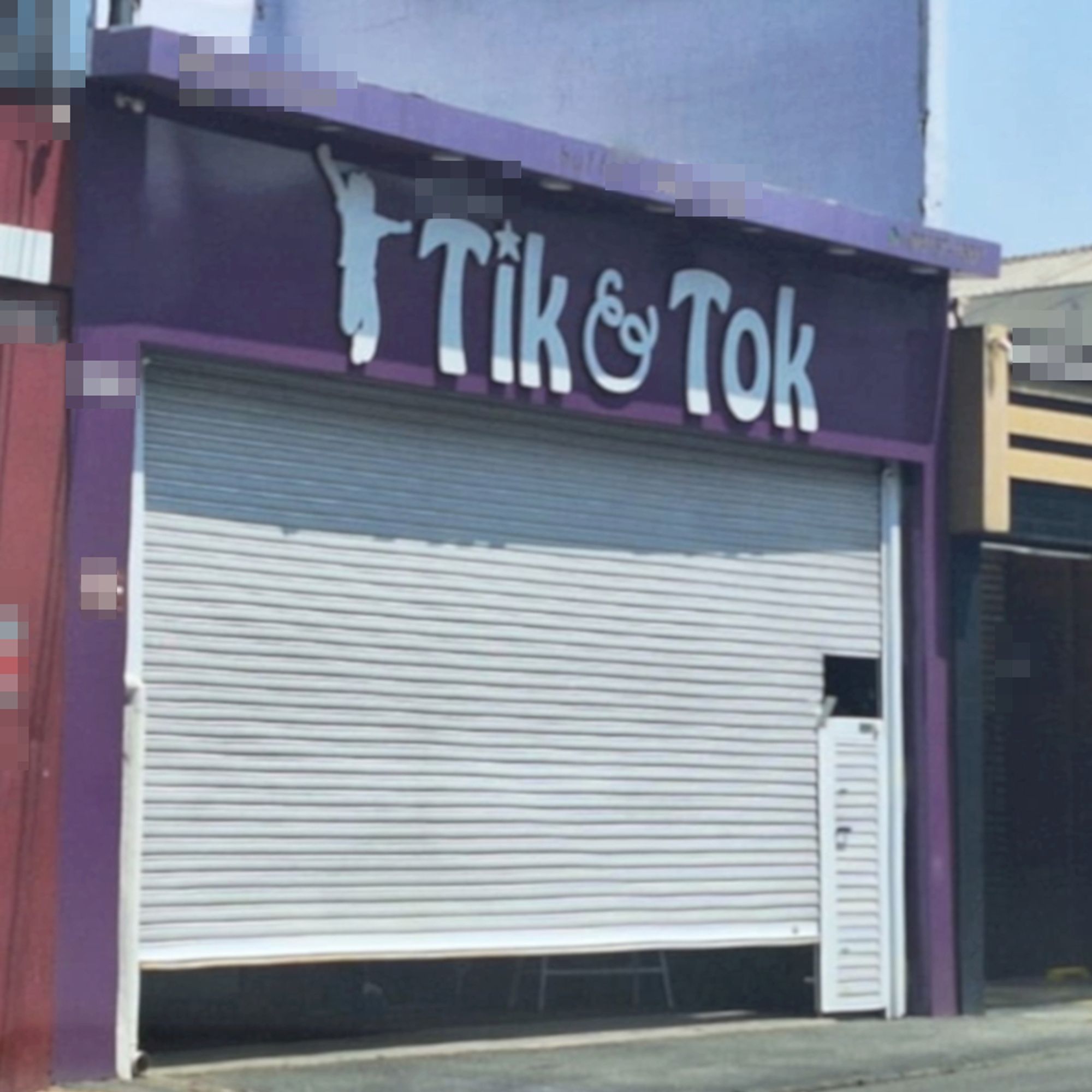 Uma fachada de uma loja com detalhes roxos e portão branco praticamente fechado, no topo se vê a silhueta de uma criança ao lado dos dizeres Tik & Tok