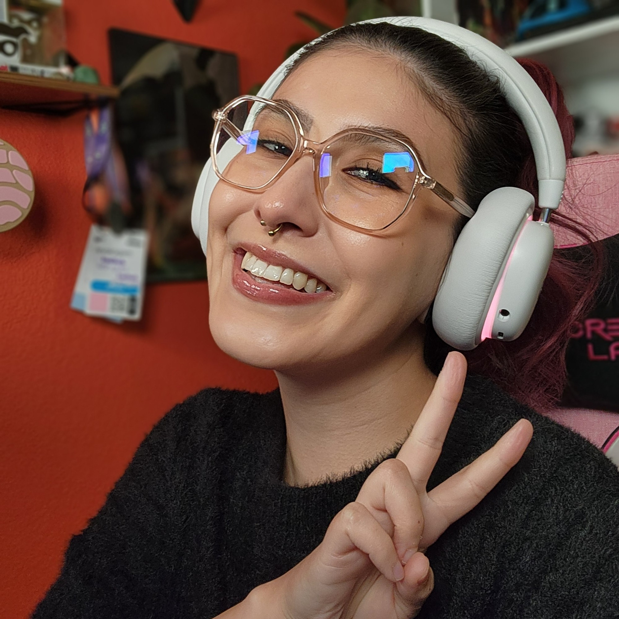 Bailee, smiling and posing with peace sign up. Her red hair is up in a ponytail and she is wearing a black fuzzy sweater and glasses.