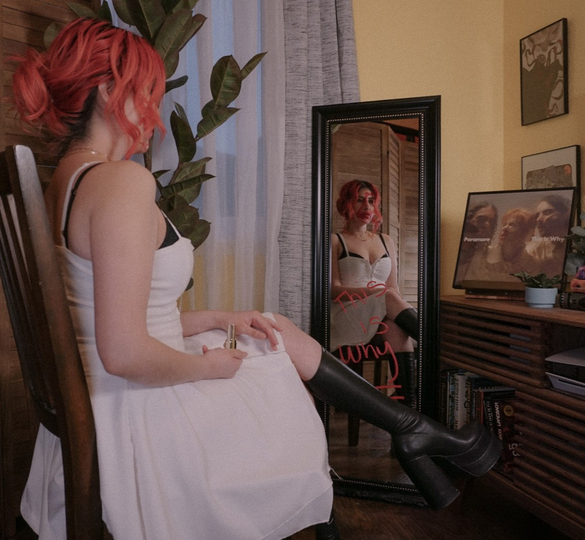 Bailee re-creating the end image of the This is Why music video by Paramore. She is sitting, with red lipstick smeared all over her face, in front of a mirror with the words "This is Why" written in red on it. She is wearing a white dress and black knee high boots.