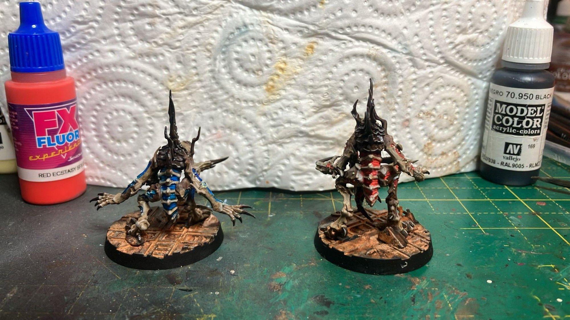 Two genestealers. Both with brown armour platers, bone skin. One with blue accents the other vibrant red. Back shot.