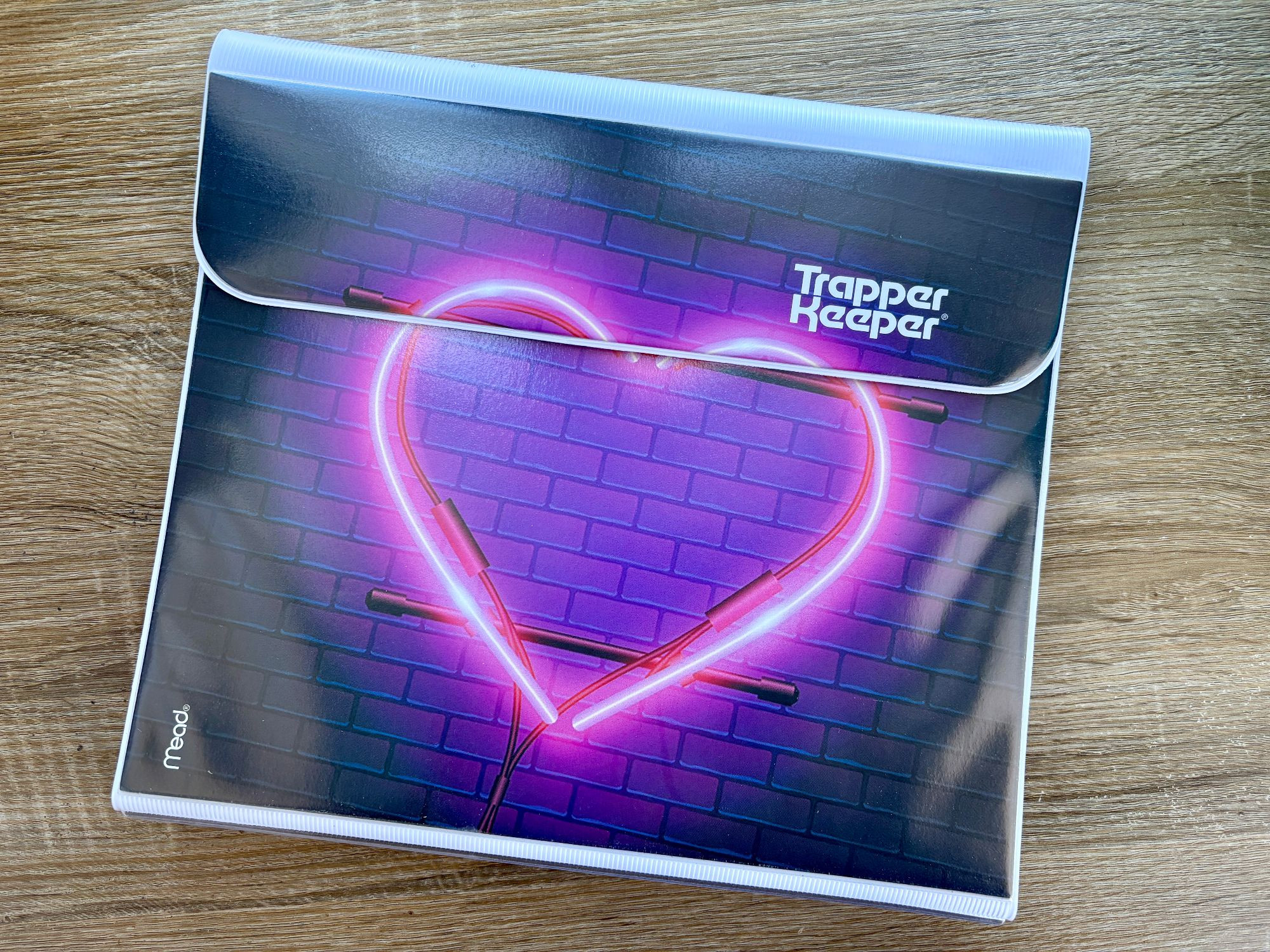 A brand-new Trapper Keeper with an illustration of a neon-pink heart on a purple brick wall