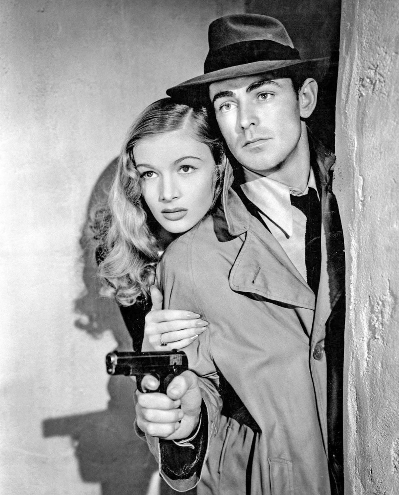 Veronica Lake behind Alan Ladd holding a gun in a promo photo for This Gun for Hire.