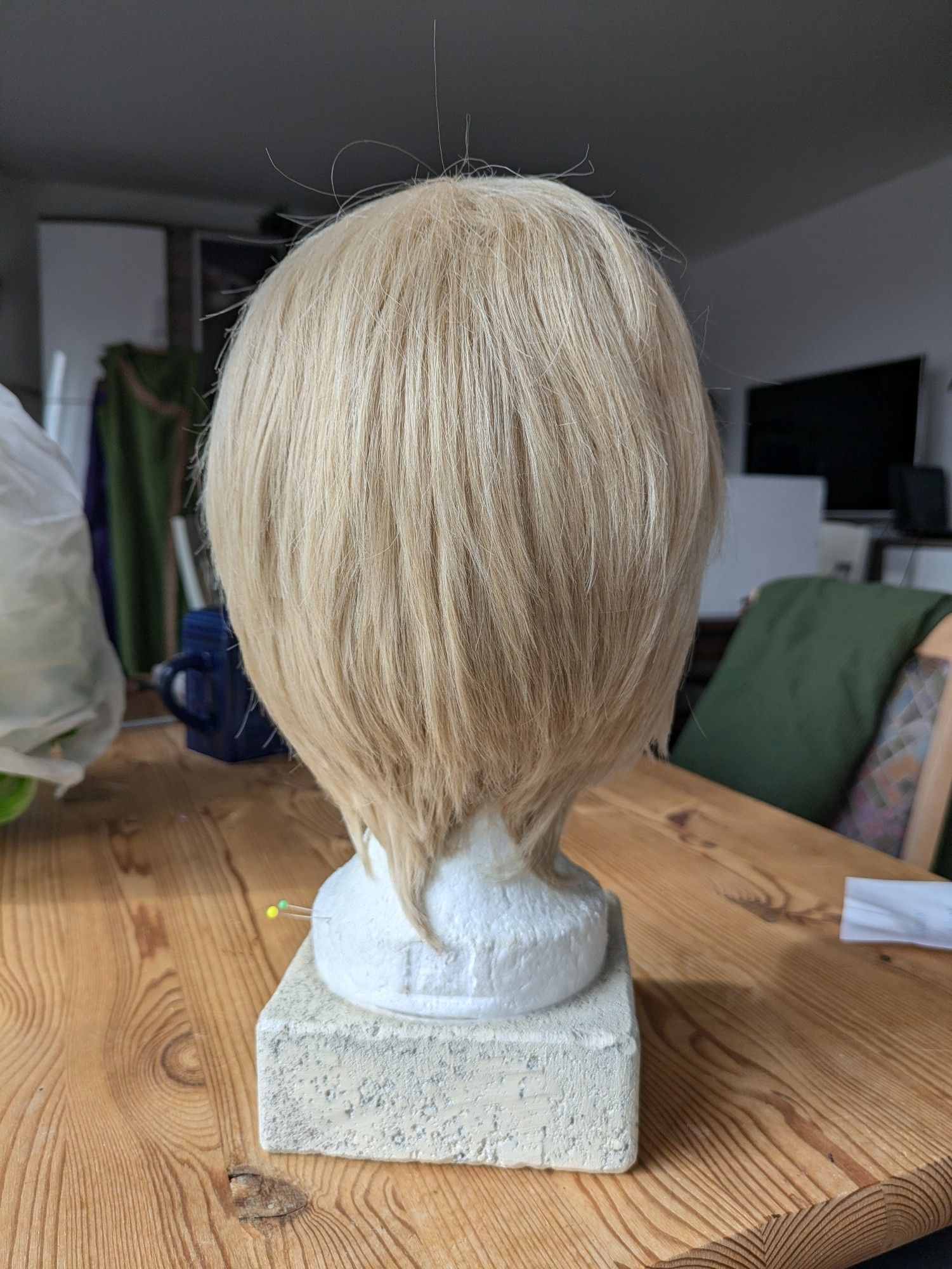 A short sandy blonde wig on a wig head, back view