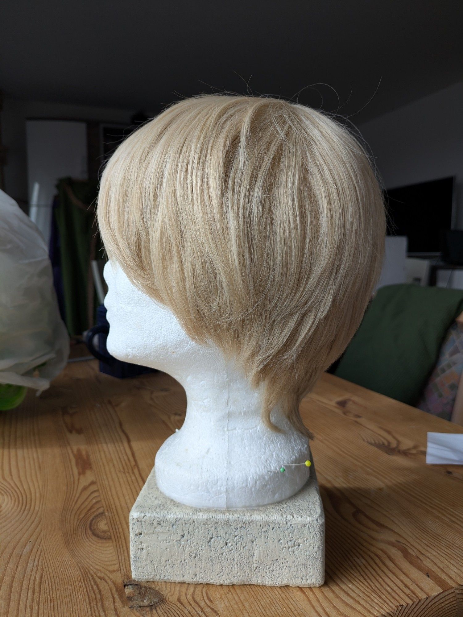 A short sandy blonde wig on a wig head, facing sideways