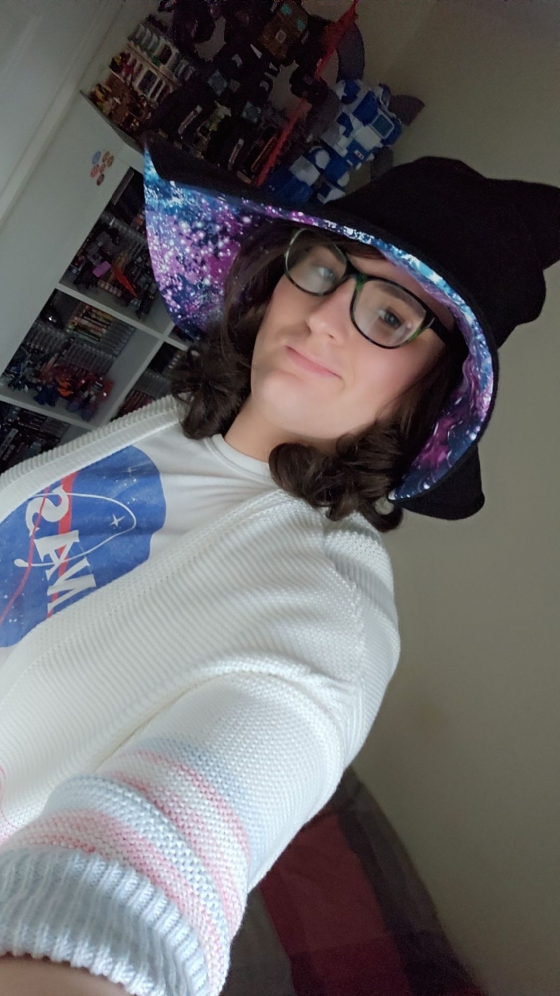 Jess wearing a witch hat, a Nasa T-shirt, and a white cardigan with baby pink and blue striping on the sleeves.