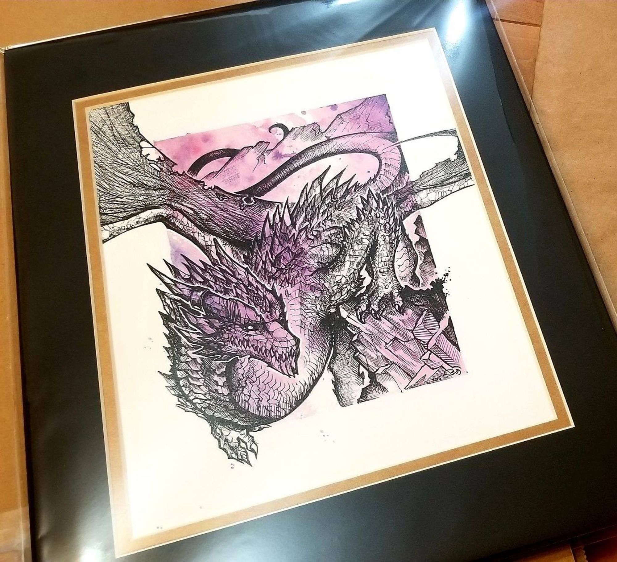 A crystalline black-ink-hatched dragon winding its way down a rocky outcrop, wings unfurled. The background is purple and splotchy with a prominent white border. There is a black mat around it with a gold inner trim. The whole thing is a bit glossy from the plastic sleeve it's in.