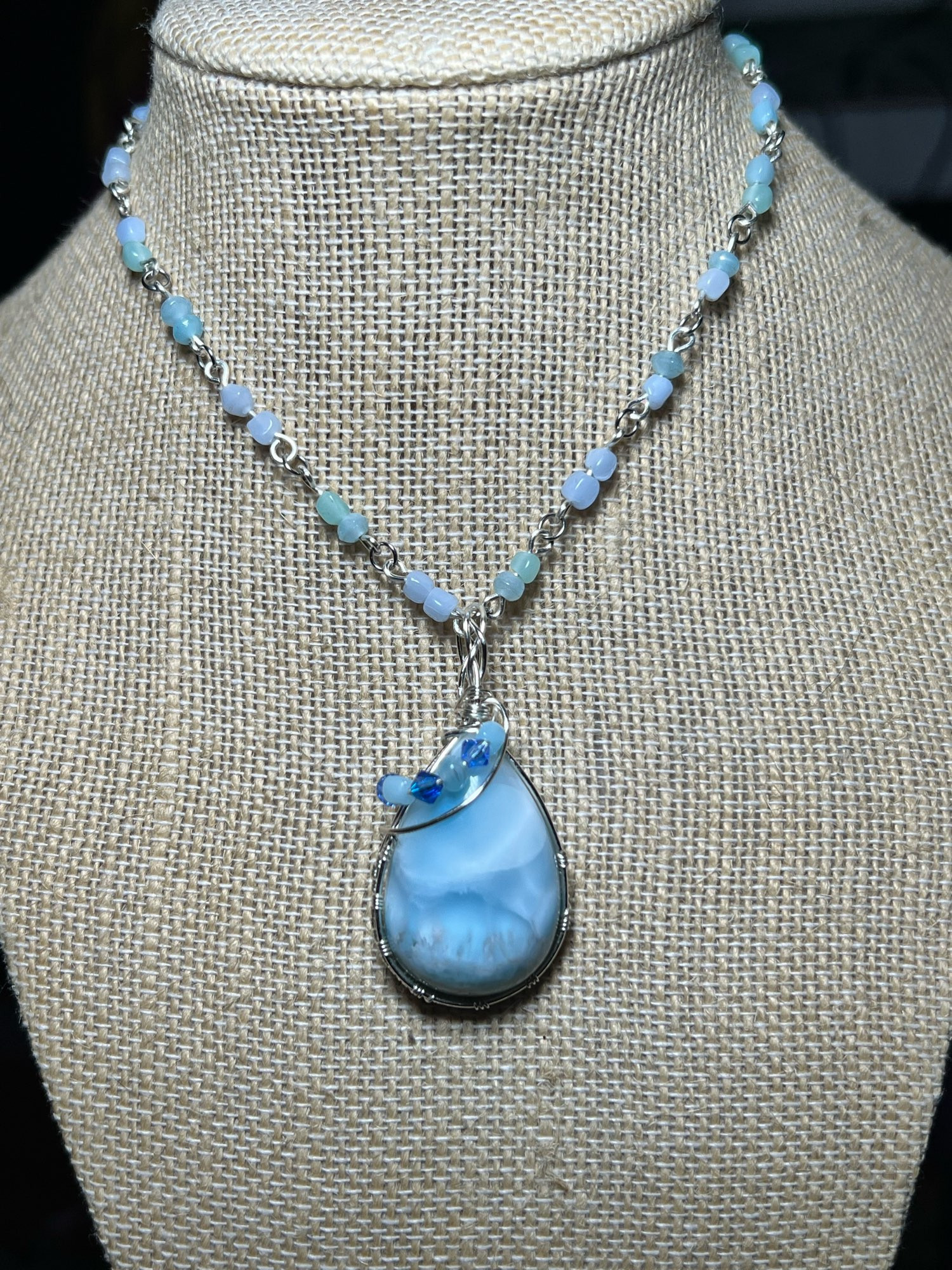 A necklace made with blue beads to create a chain, the center pendant is tear drop shaped blue Larimar stone wrapped in silver colored craft wire