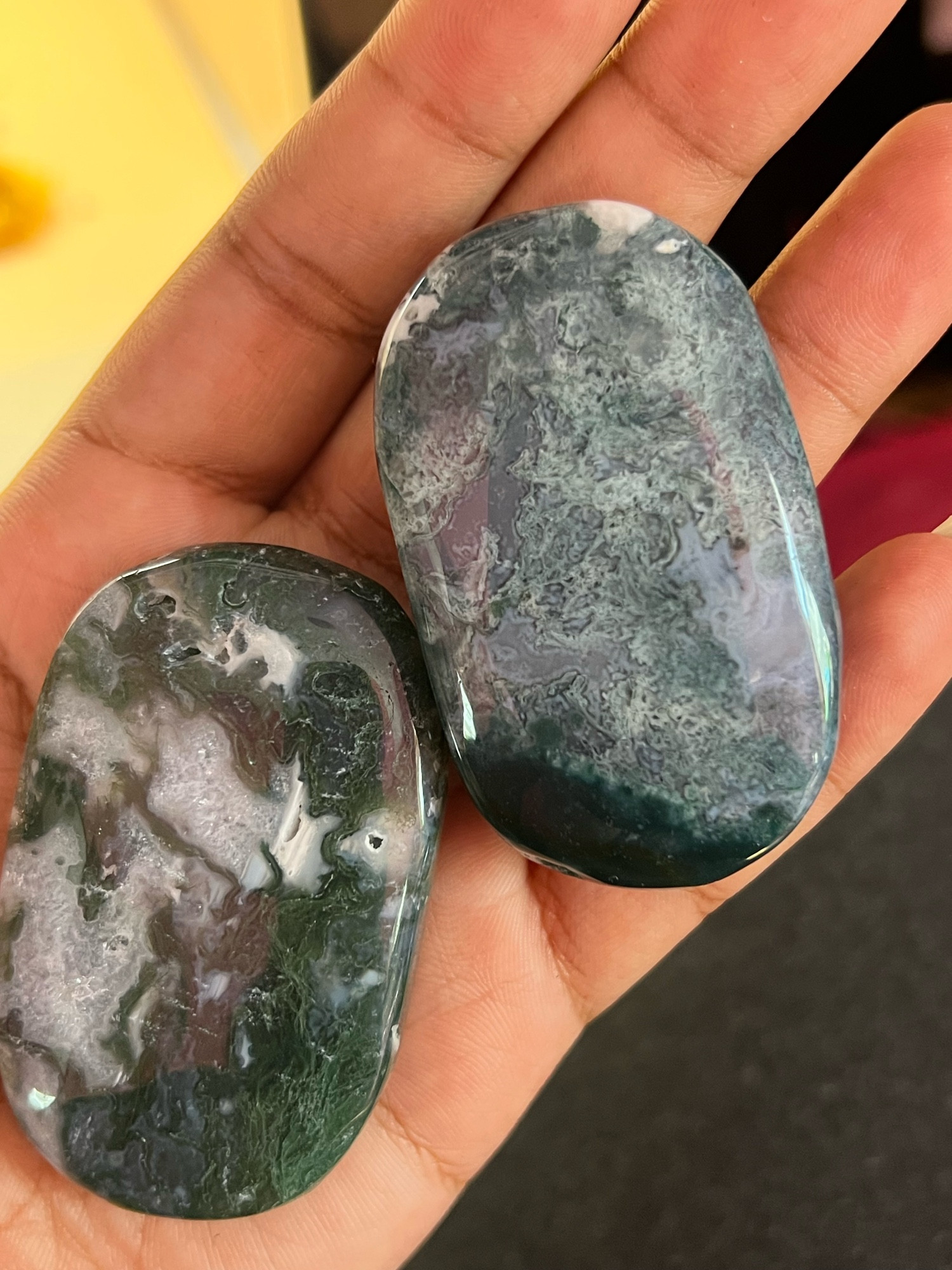 Two oval like polished rock/stones held in a hand, with hues of deep & light green, iPhone and some murky pearlescent