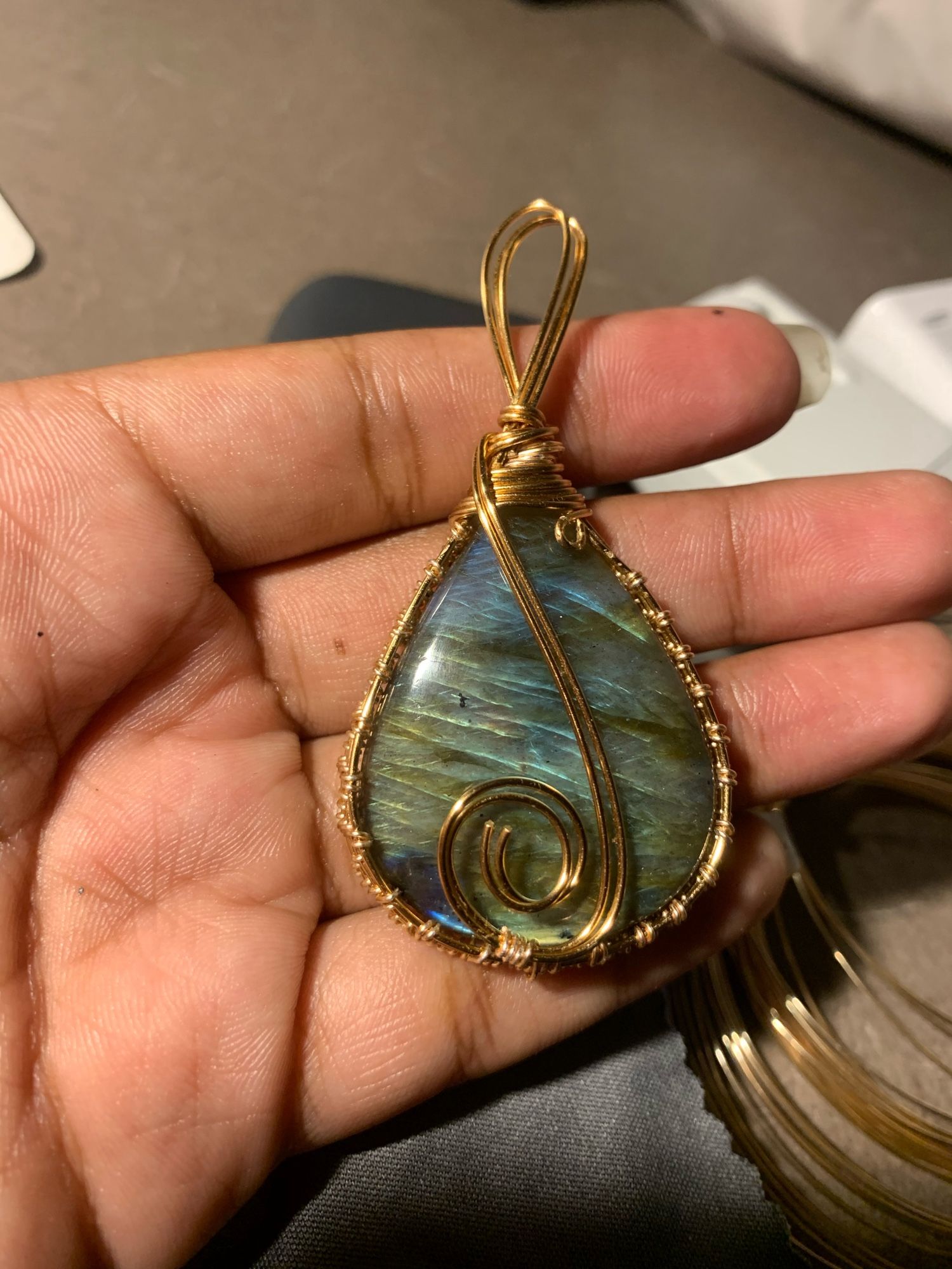 A greenish golden & blue medium tear drop labradorite wrapped in copper wire, with a swirl showcased on the bottom held in a hand