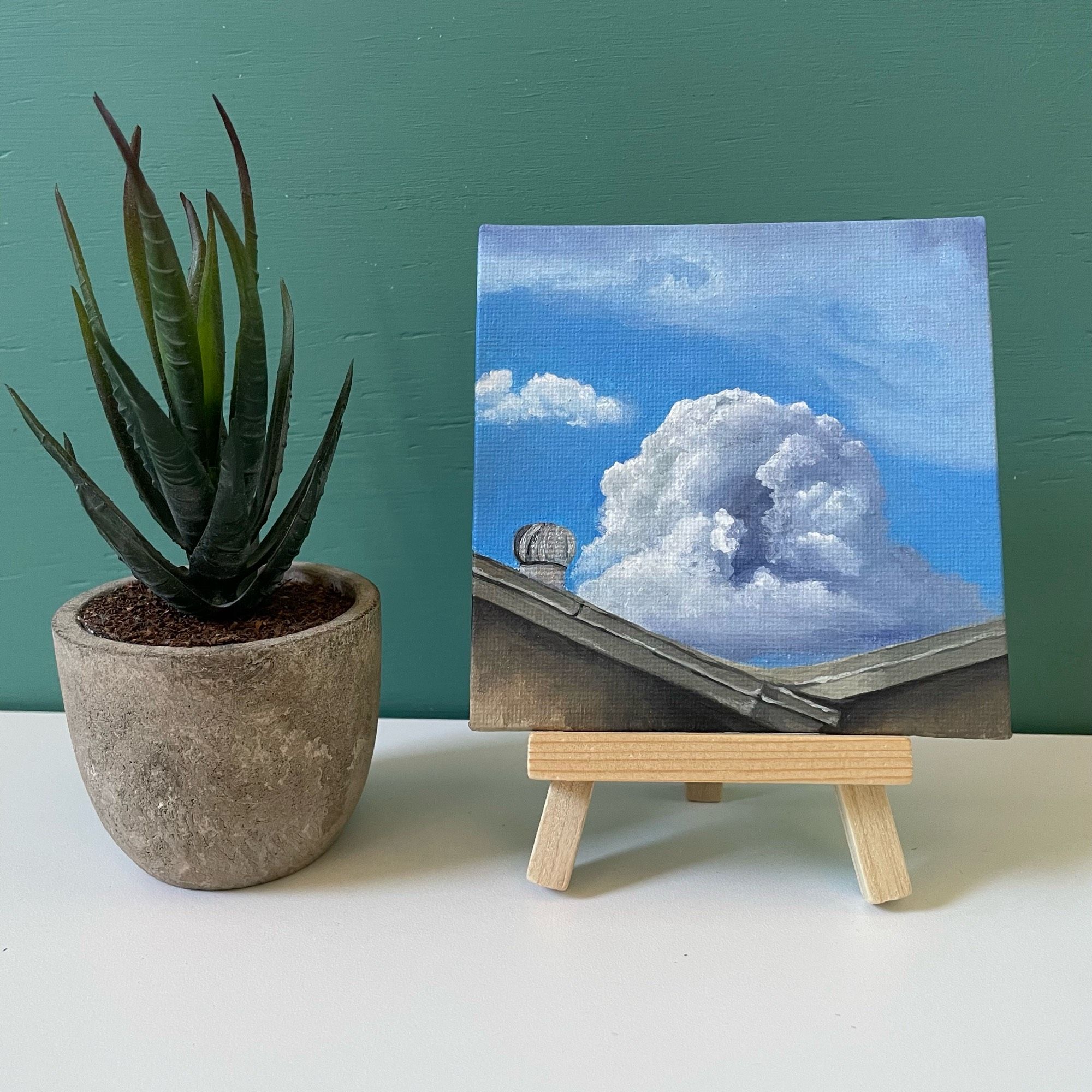 Mini painting of cloud next to fake plant