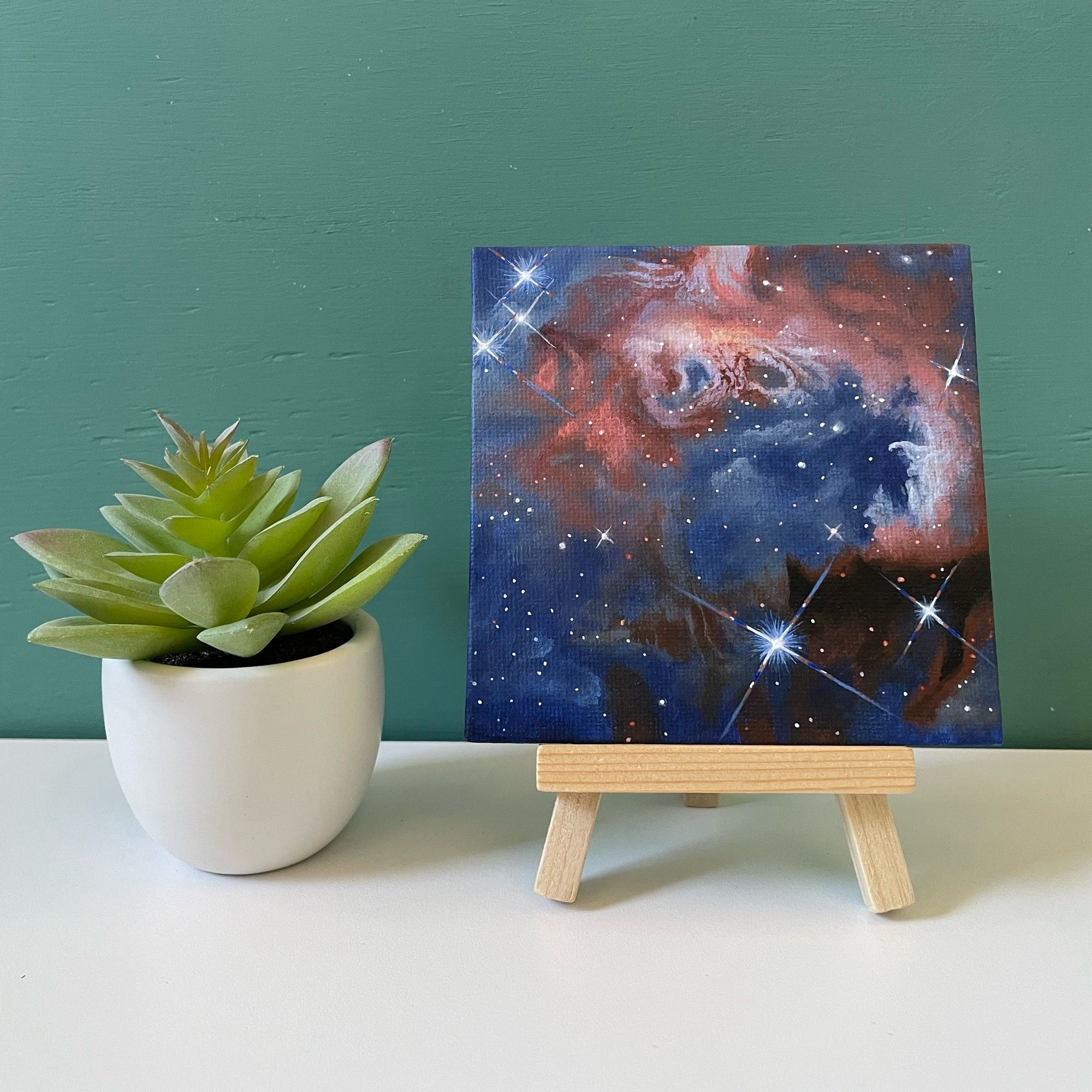 Mini nebula painting on easel next to fake succulent