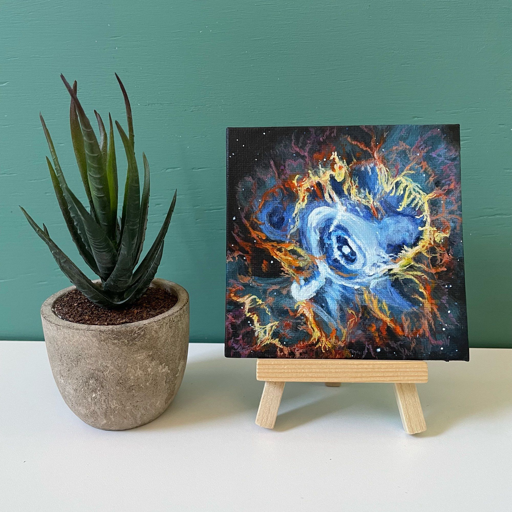 Mini painting of Crab Nebula on easel next to fake plant