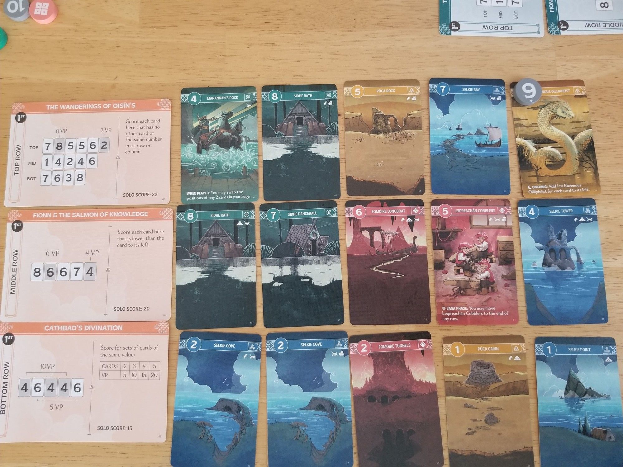 A game of Tír na nÓg in progress. A tableau of colorful cards depicting scenes from Irish mythology, three rows of five cards each, plus scoring cards on the left side describing scoring goals.