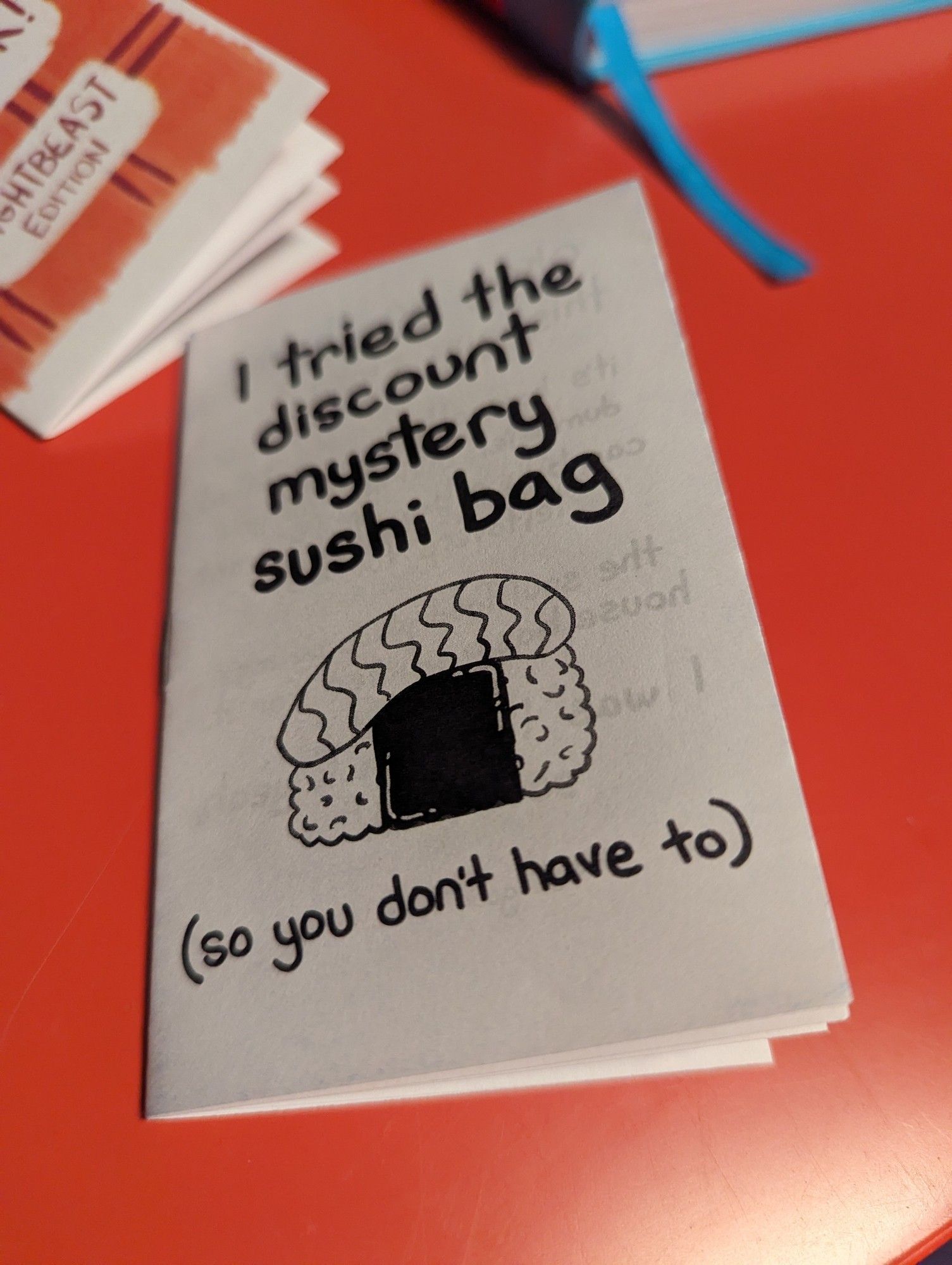 Picture of a little zine called "I tried the discount mystery sushi bag (so you don't have to) with a little drawing of a piece of nigiri on it.