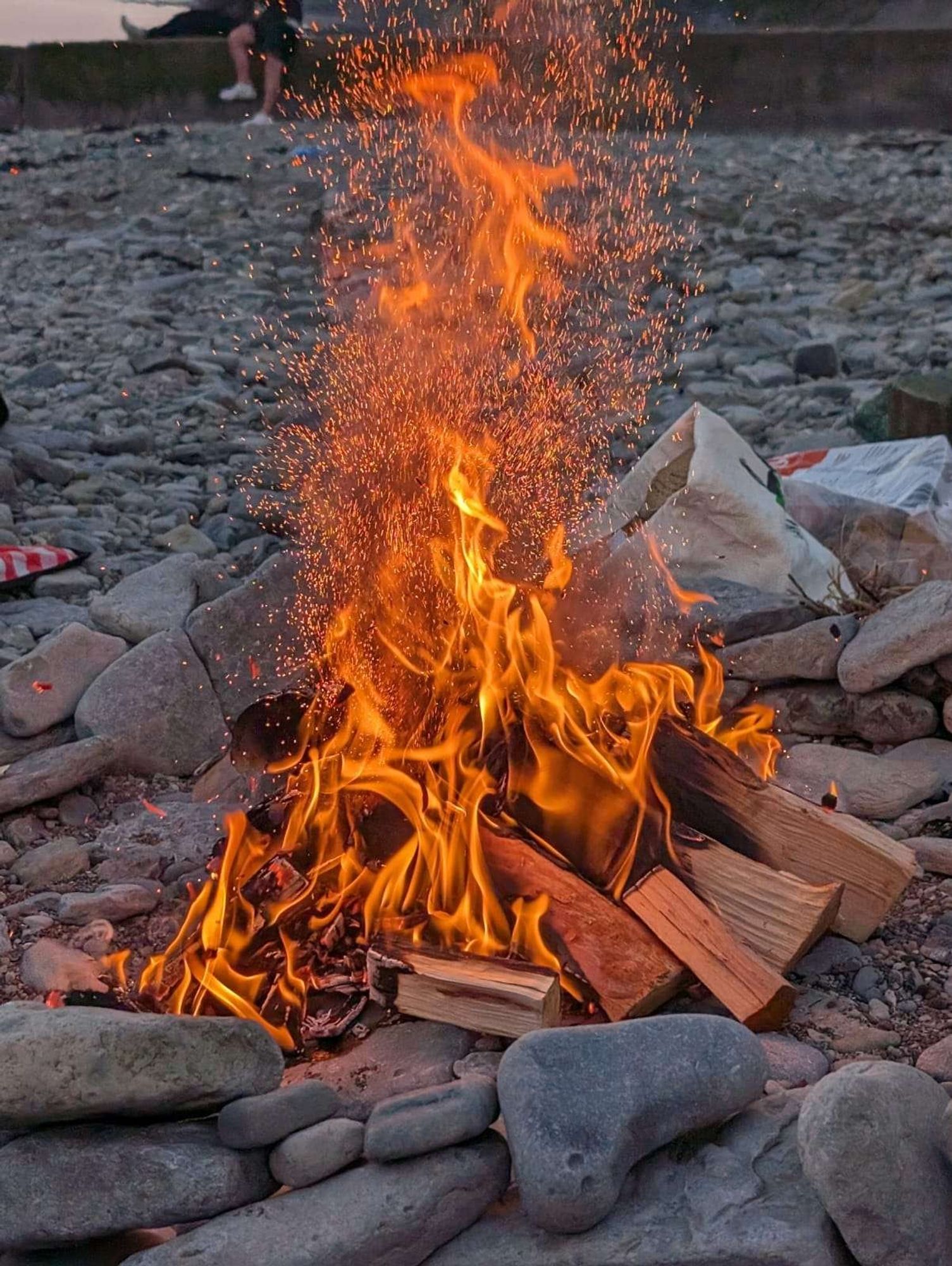 bonfire in a ring of stones on a pebbly beach. many embers are thrown up in this action shot as a limestone pebble inside the fire explodes (the water inside this porous rock has expanded from the heat, causing it to pop)