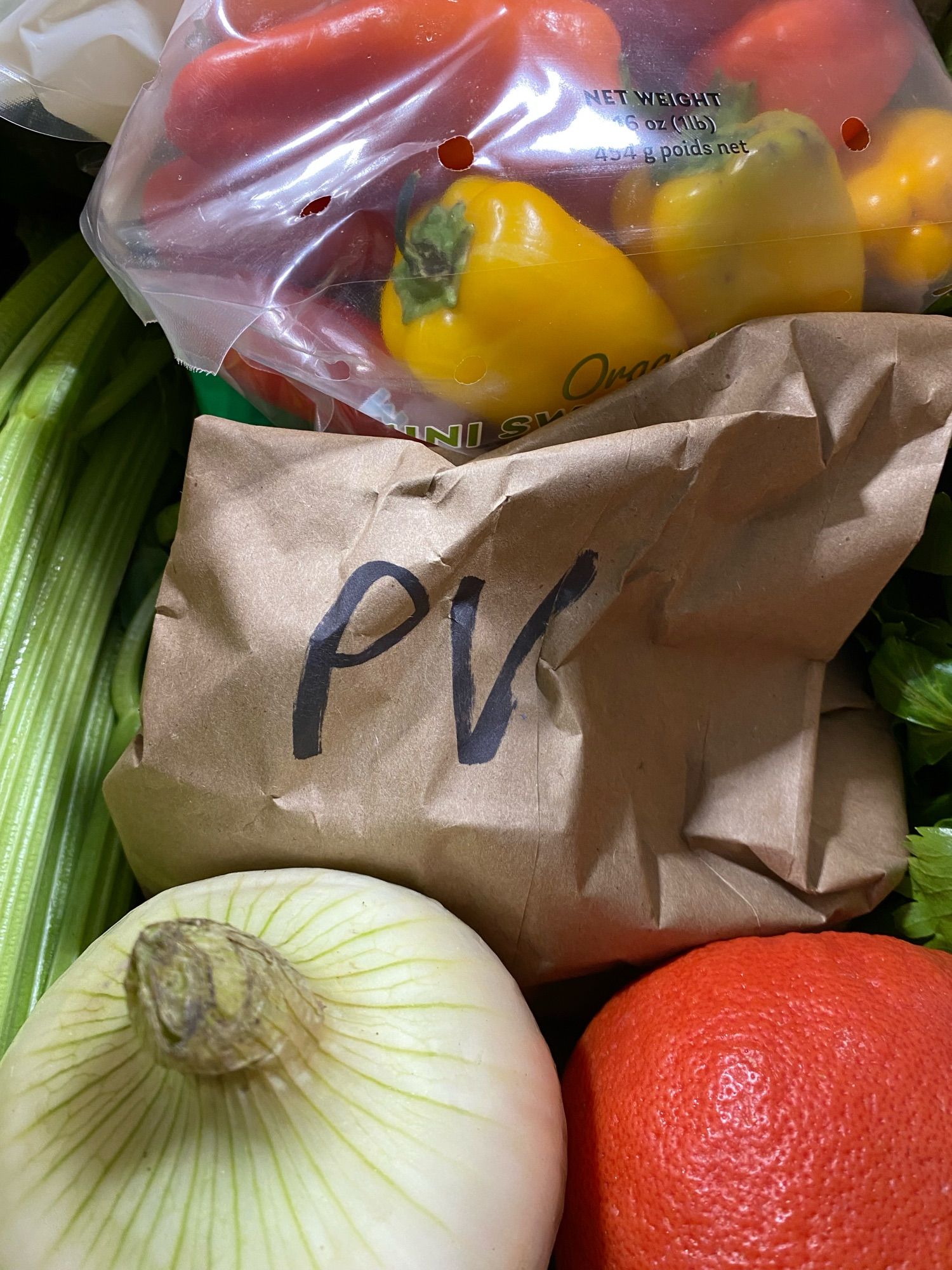 A collection of veggies surrounding a brown paper bag labeled “pv”