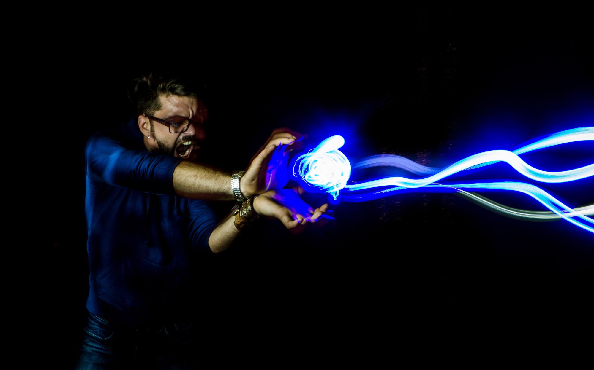 Lightpainting of a man standing in darkness shooting blue energy from his hands in Kamehameha (Dragon Ball) fashion.