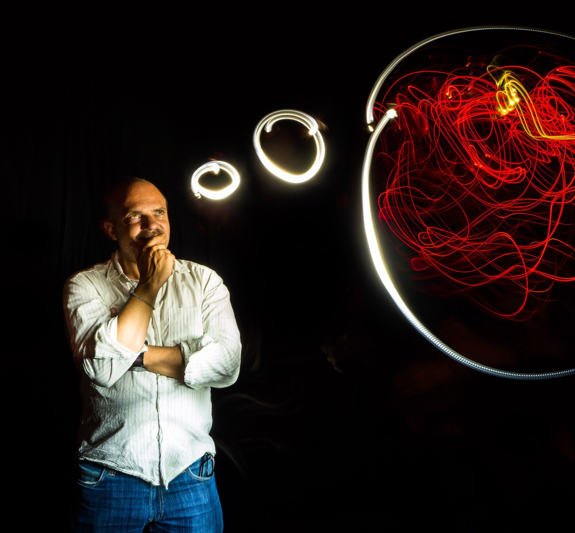 Lightpainting of a man in front of a black background thinking. There is a  though bubble above his head painted in light.