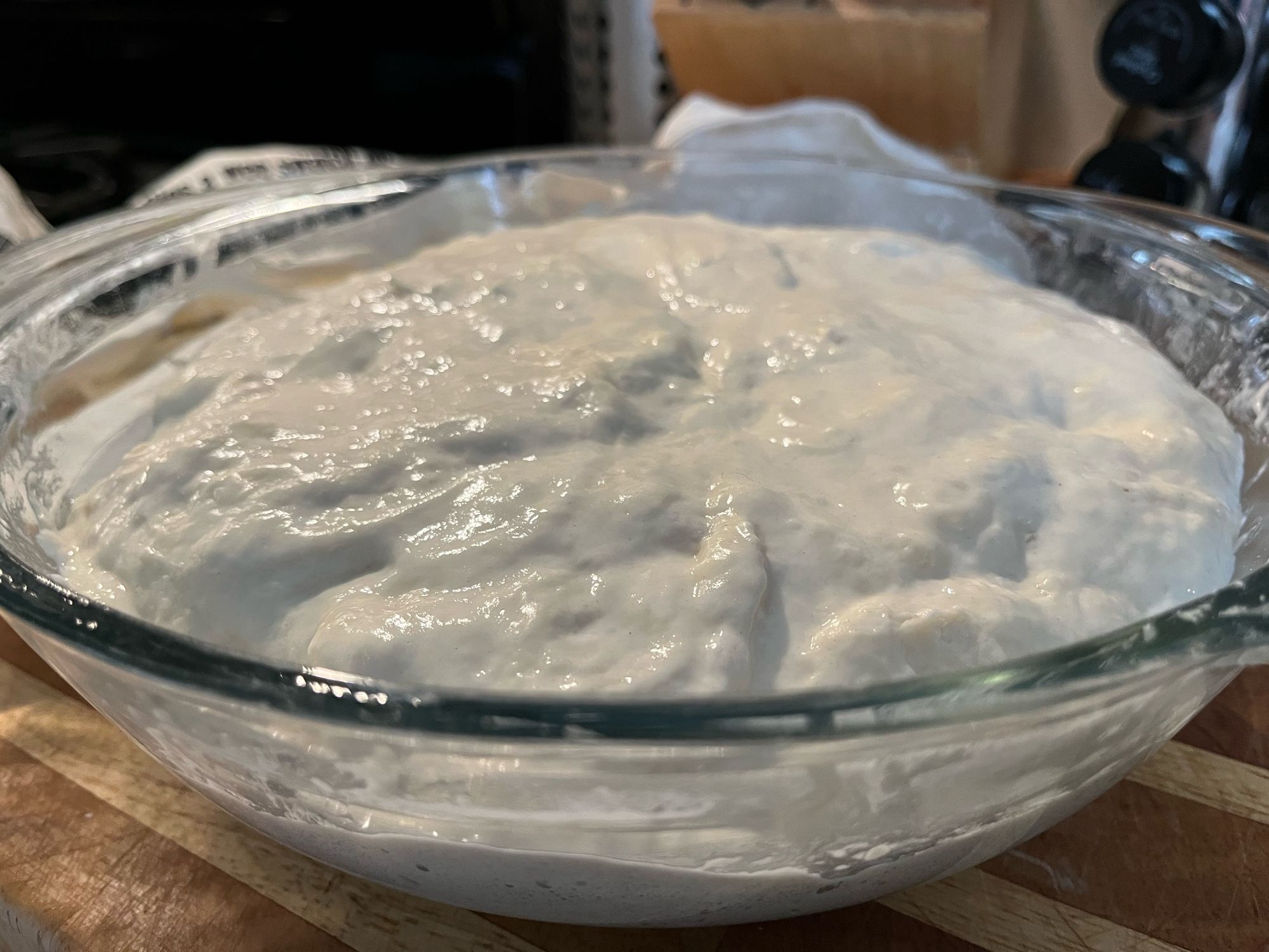 A glass bowl containing bread dough that’s doubled in size after its first proof.