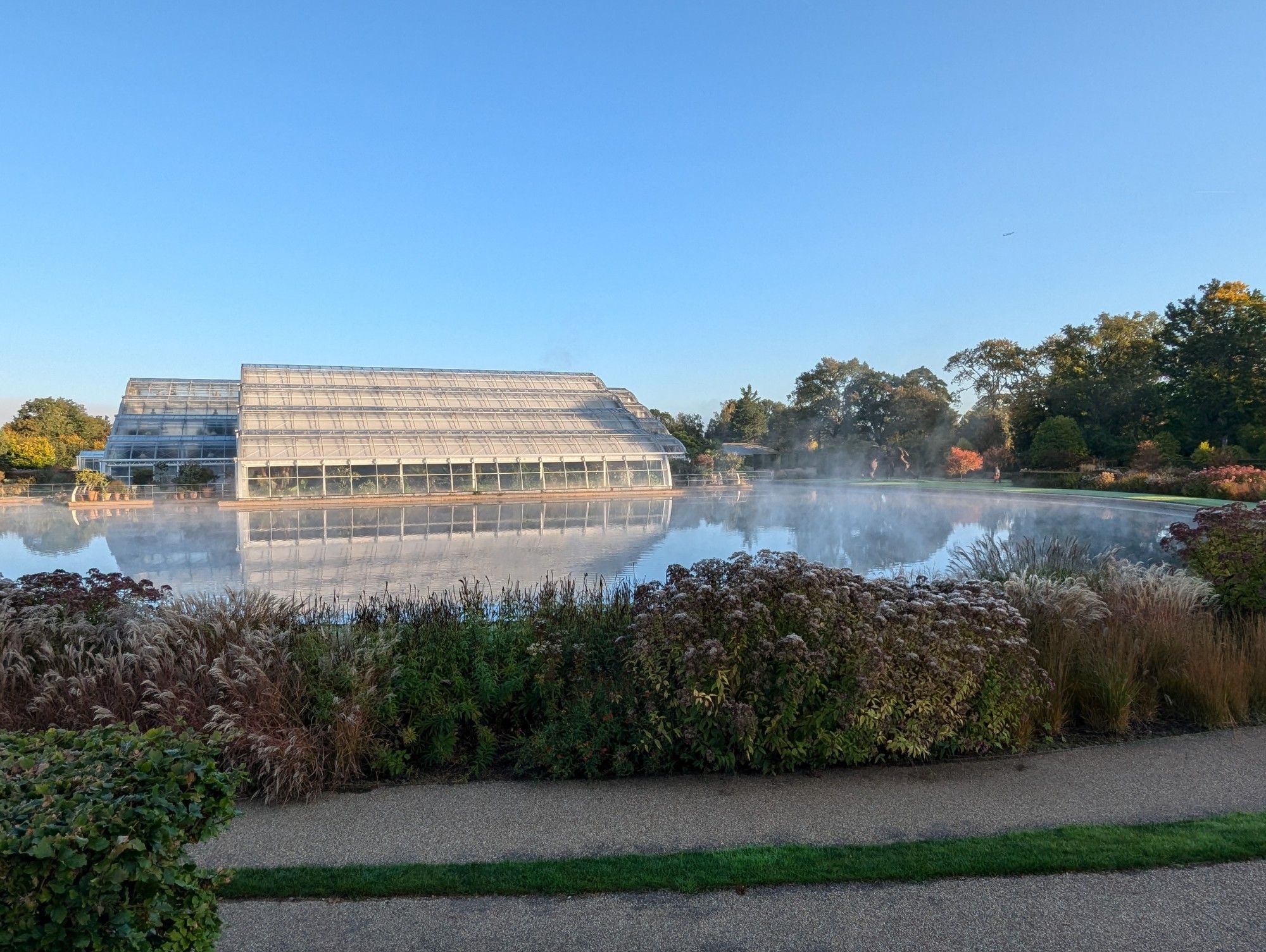 The Glasshouse and lake at RHS Wisley with a clear blue sky behind them