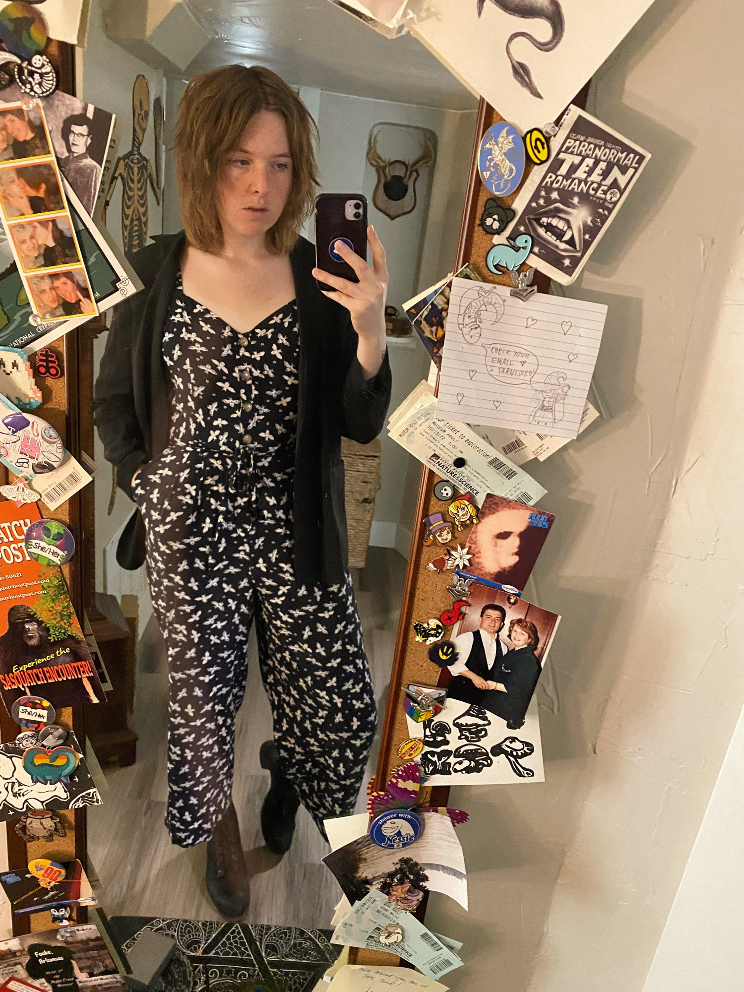 Mirror selfie of Nessie in a Bee themed jumpsuit, a light, black blazer, and heels. It’s hair is messy and it has one hand in its pocket