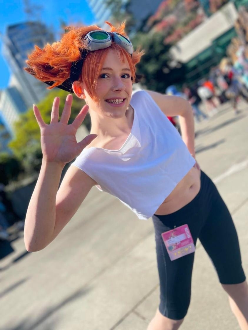 A photo taken in the courtyard of the convention of a young woman in cosplay of Edward from Cowboy Bebop, looking enthusiastically at the camera with a wave and soft sunlit glow. Photo taken by LarryBoiii on instagram!