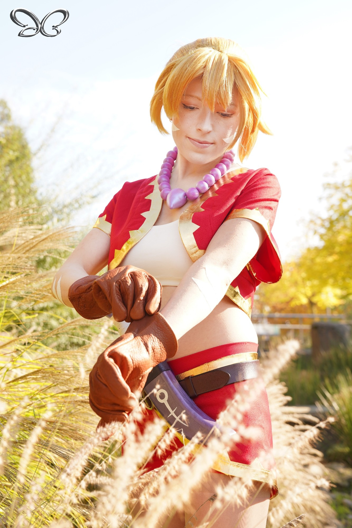 A soft image with golden light of a young woman cosplaying Kid from the video game Chrono Cross. She appears to be pulling on a pair of chunky leather gloves while stepping through tall whispy grass. Photo taken by Images_by_jc on Instagram.