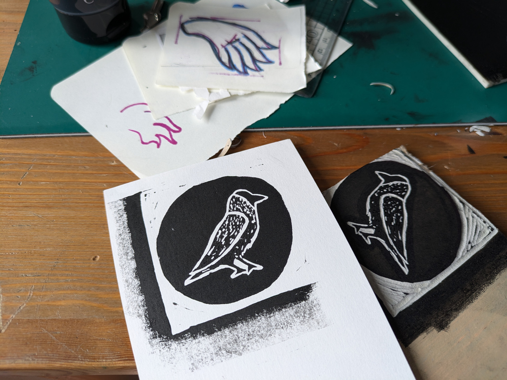 A photo of a linocut block and the corresponding print, depicting a stylised jackdaw. The print is mostly black, with the outline of the bird in white.