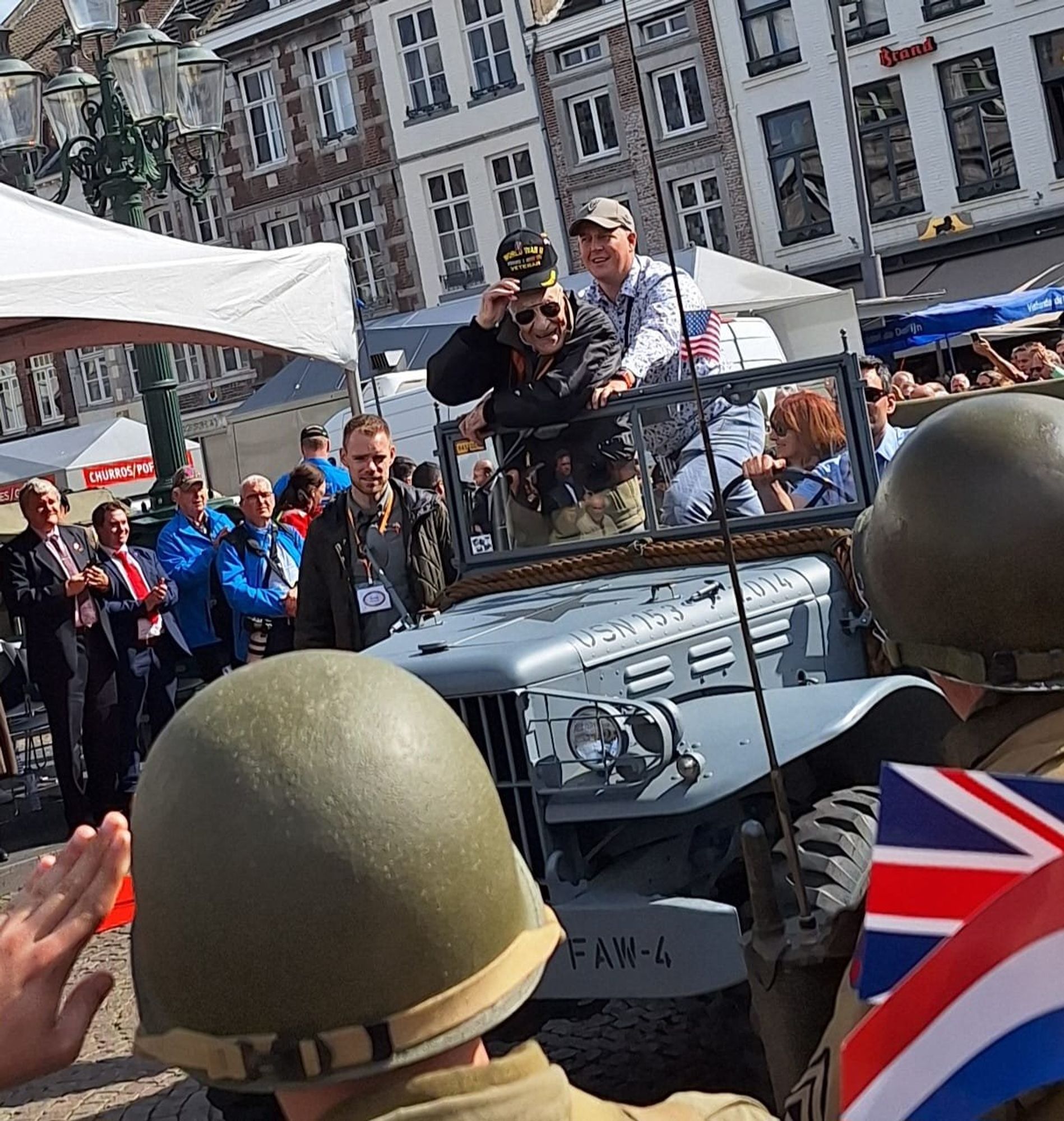 Veteraan tijdens de Liberation Parade, staand op een jeep, omringd door zwaaiende, klappende en saluerende mensen.