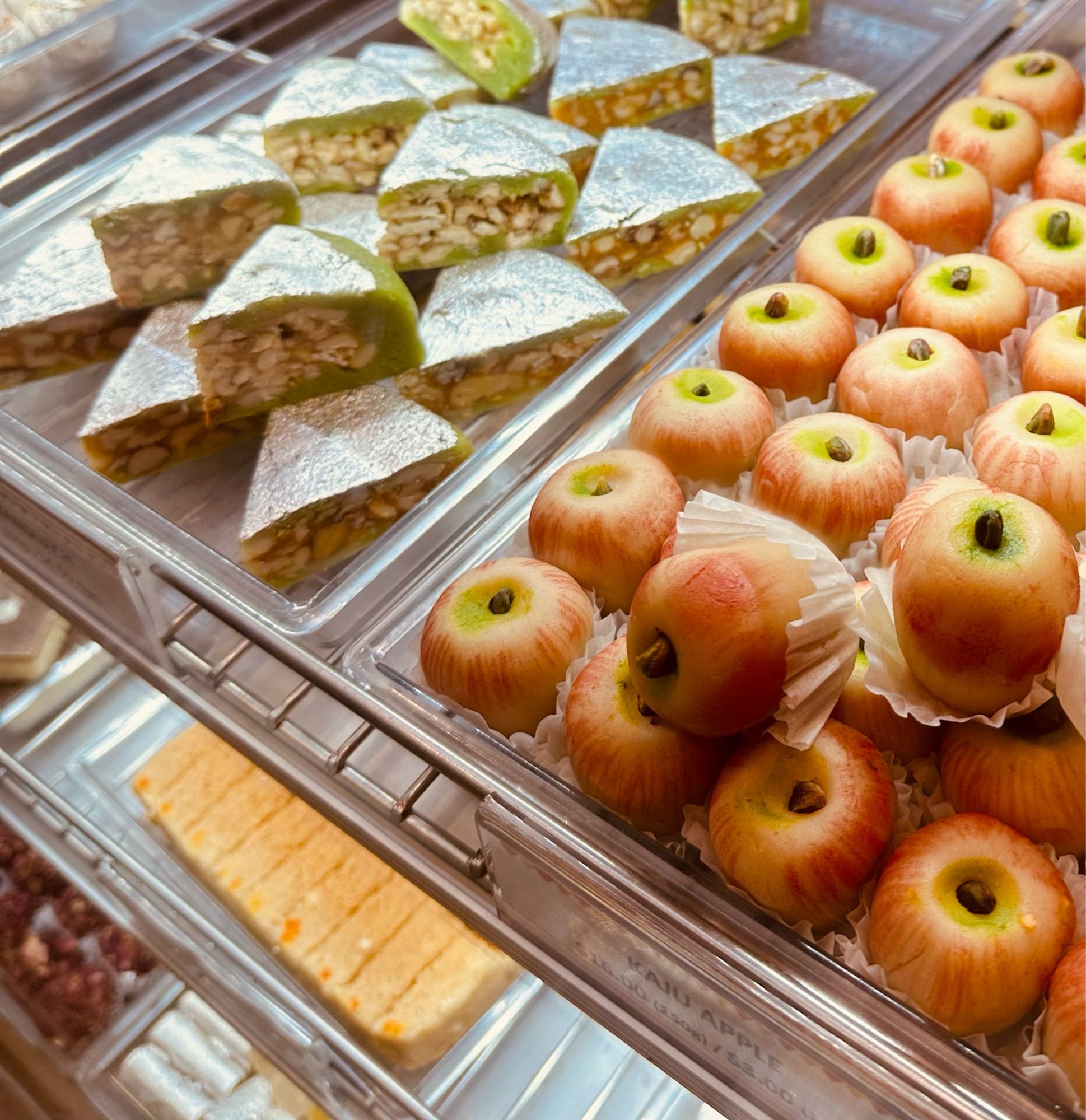 Cabinet full of sweet desserts: triangle shaped  slices and tiny apple shaped confectionary.