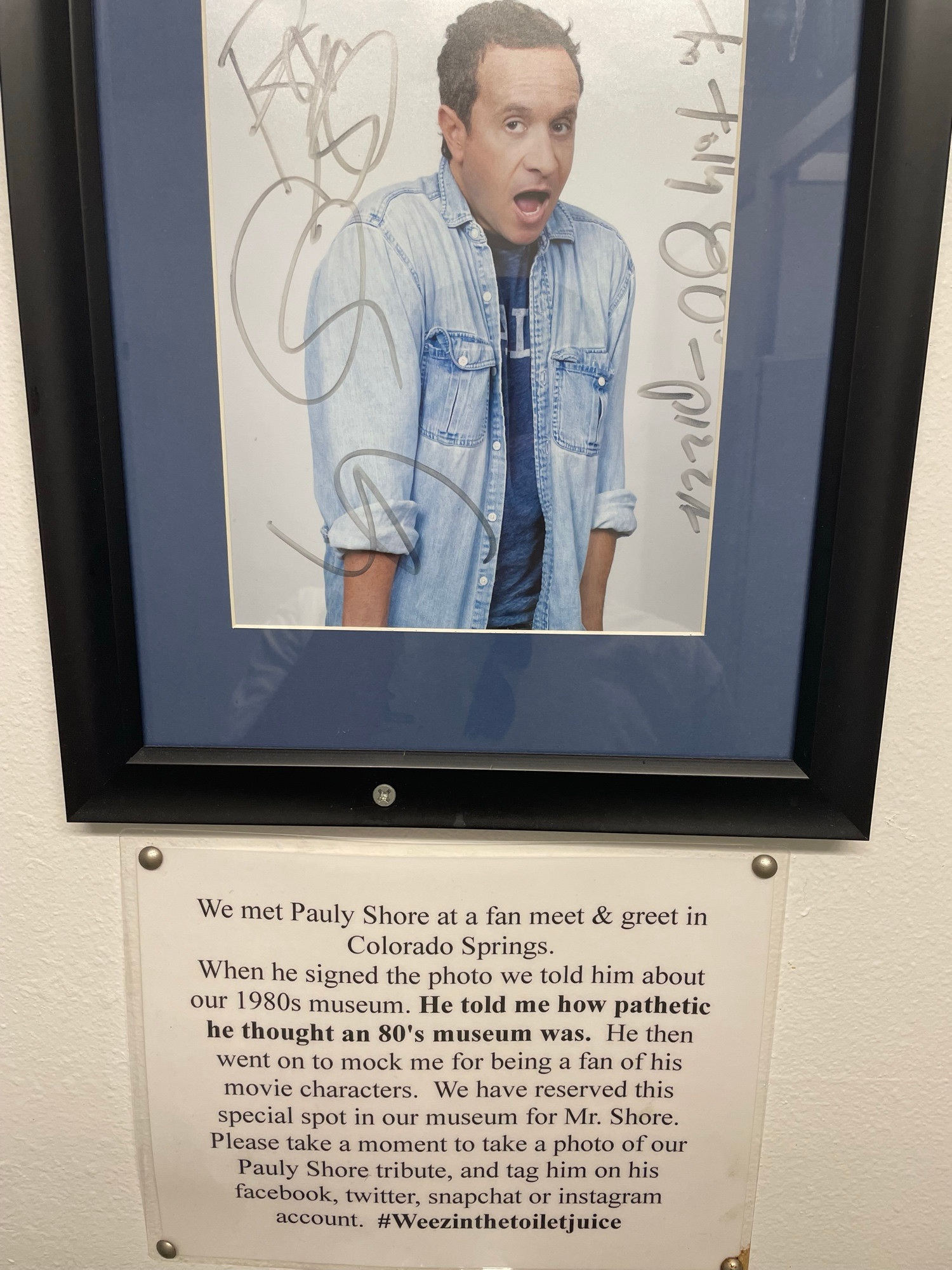 Signed photo of Shore above a sign reading “We met Pauly Shore at a fan meet & greet in
Colorado Springs.

When he signed the photo we told him about our 1980s museum. He told me how pathetic he thought an 80's museum was. He then went on to mock me for being a fan of his movie characters. We have reserved this special spot in our museum for Mr. Shore.
Please take a moment to take a photo of our Pauly Shore tribute, and tag him on his facebook, twitter, snapchat or instagram account. #Weezinthetoiletjuice”
