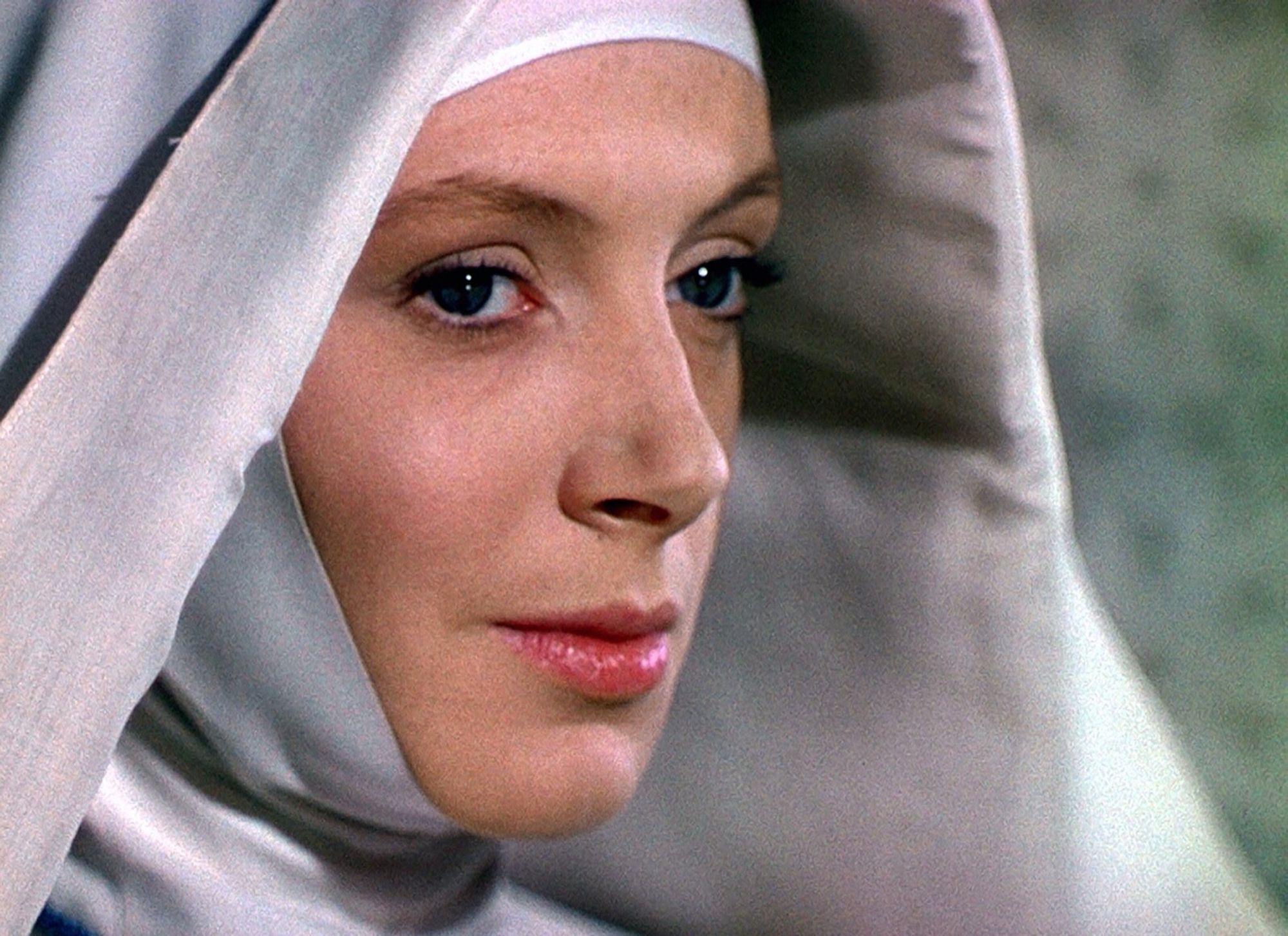 Color photo of Deborah Kerr from Black Narcissus (1947). It is a closeup of her wearing an off-white colored nun’s habit, only the front of her face is visible. She is looking to the right through piercing dark eyes past the camera with a slightly bemused expression.