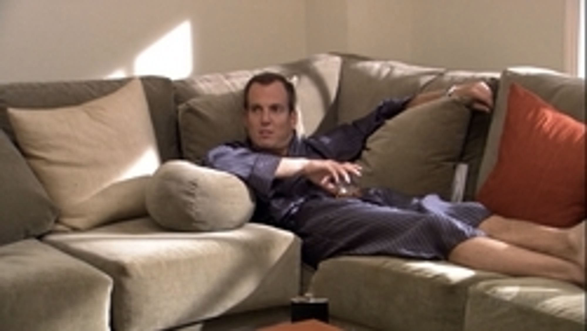 GOB Bluth on a couch in a blue bathrobe, lifting his head curiously, as though he's misleading the other person in the room.