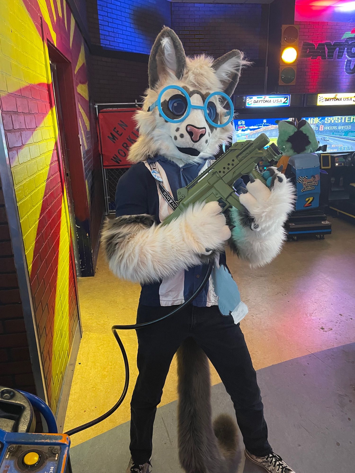 Ragdoll cat fursuiter with glasses holding an arcade machine gun.